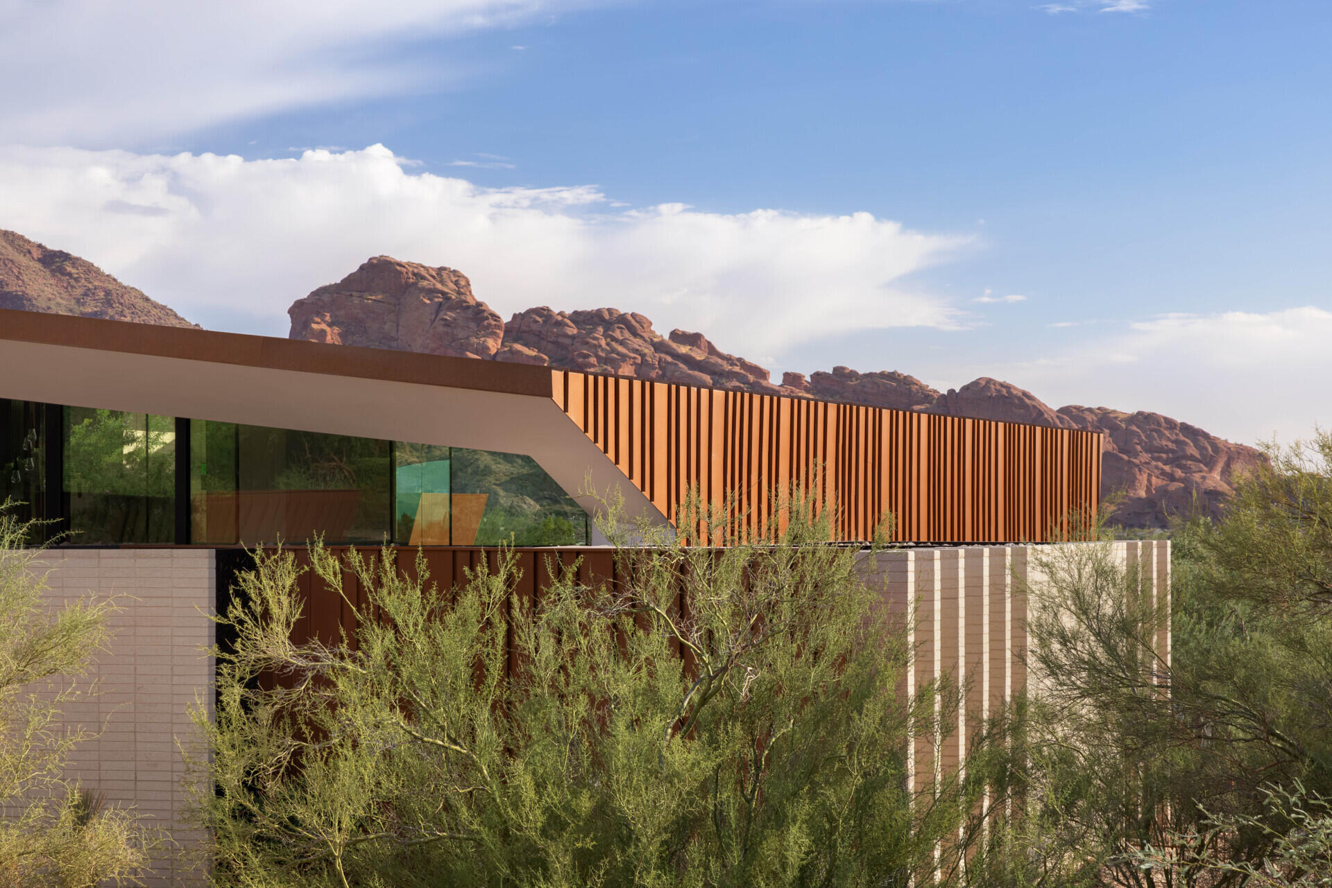 Defined by folding metal planes and rugged blasted-face masonry, the architecture of this modern house recalls the layered beauty of a geode. The weathered metal acts as a protective shell, sheltering the glass-filled interior that glows with natural daylight.