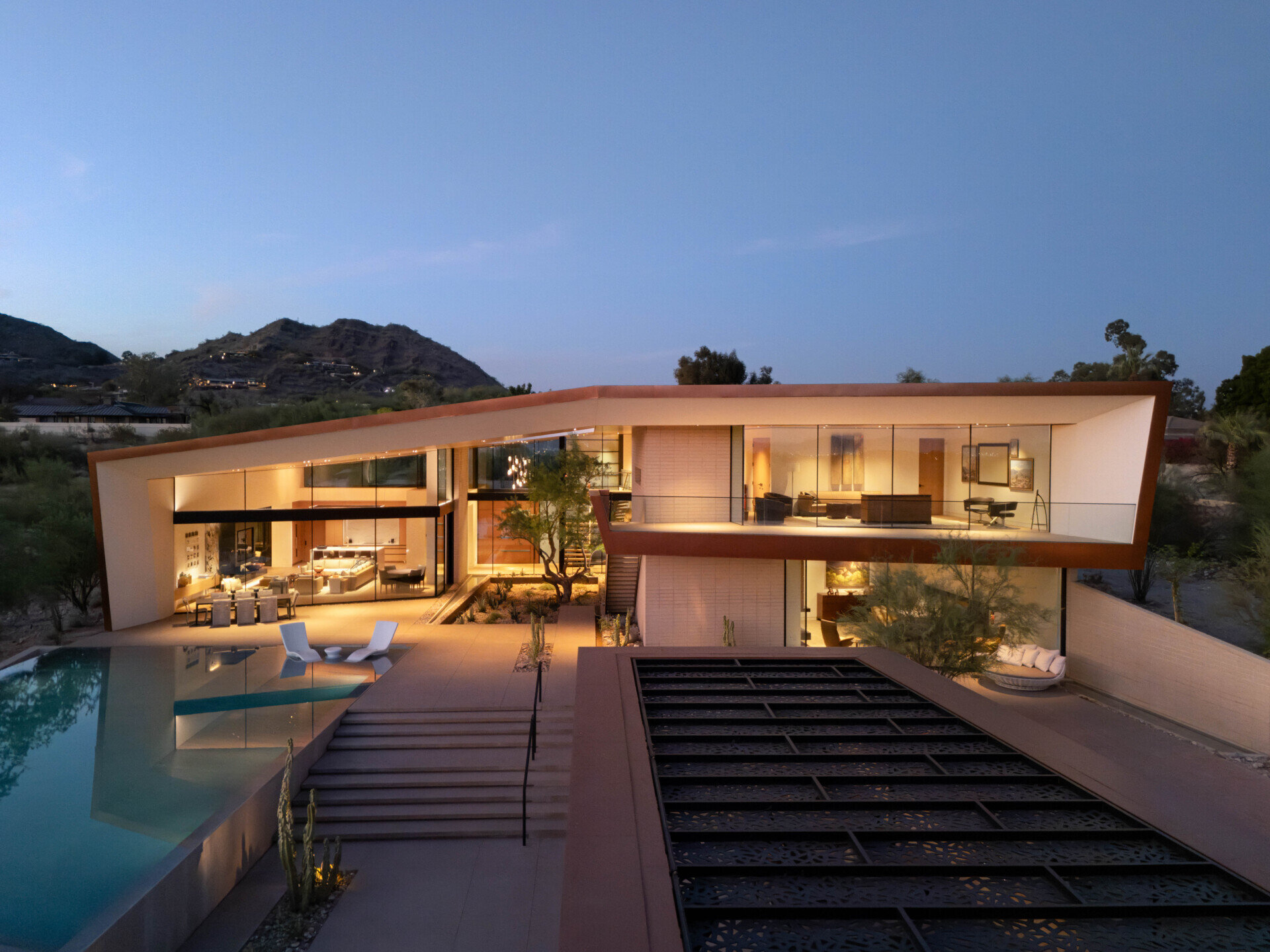 Terraces and balconies offer multiple vantage points to enjoy mountain and city views. A firepit creates a cozy evening gathering space, while an open-air cabana with a patterned metal trellis provides shade among dense vegetation.