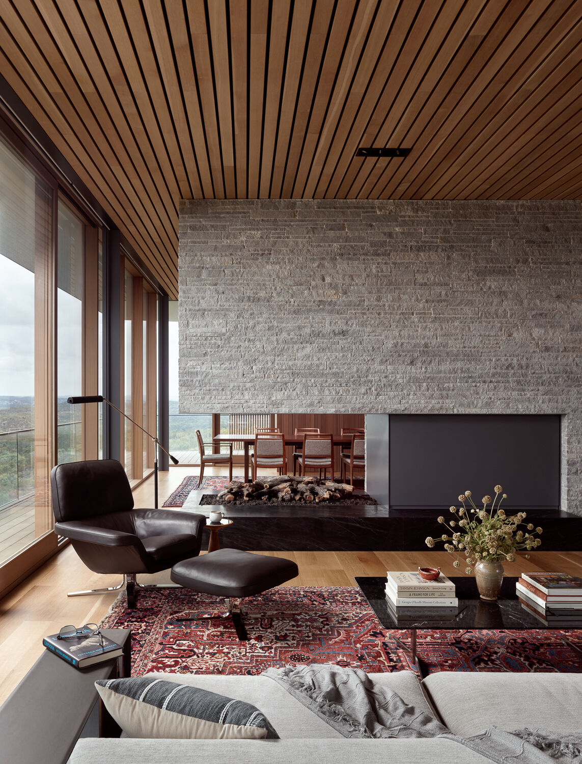 Floor-to-ceiling glazing opens dining and living spaces to natural light and views, while the fireplace, with its striking stone feature, subtly separates the living and dining areas while keeping the space connected.