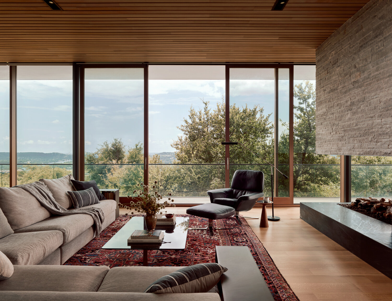 Floor-to-ceiling glazing opens dining and living spaces to natural light and views, while the fireplace, with its striking stone feature, subtly separates the living and dining areas while keeping the space connected.