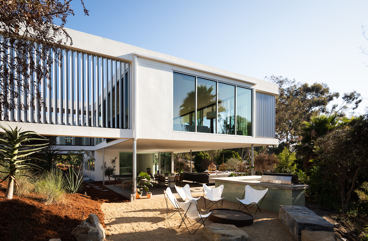 A modern house with a white exterior has a covered outdoor living room by a pool.