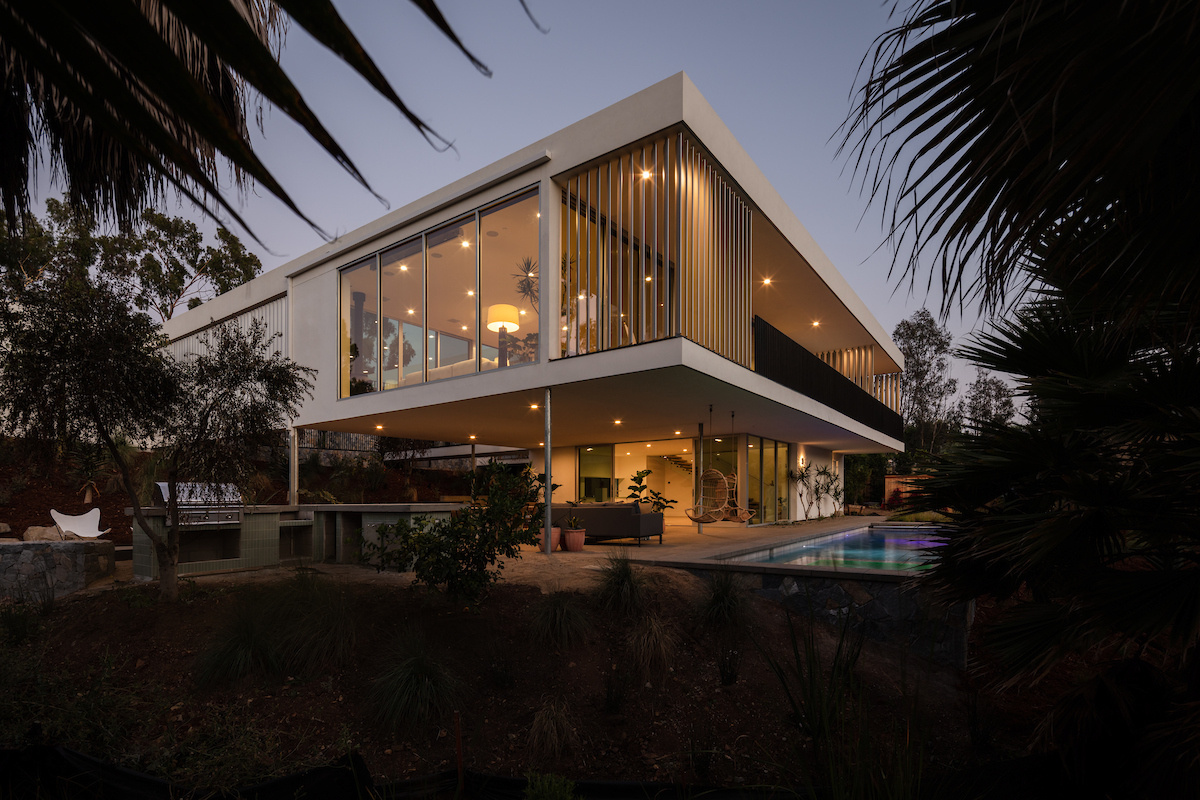 A modern house with a white exterior has a covered outdoor living room by a pool.