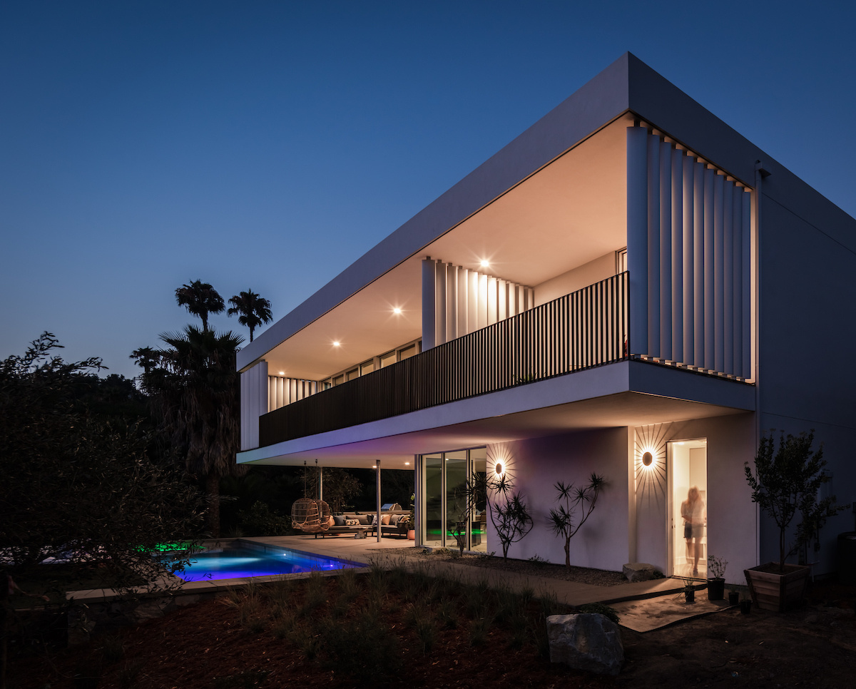 A modern house with a white exterior has a covered outdoor living room by a pool.