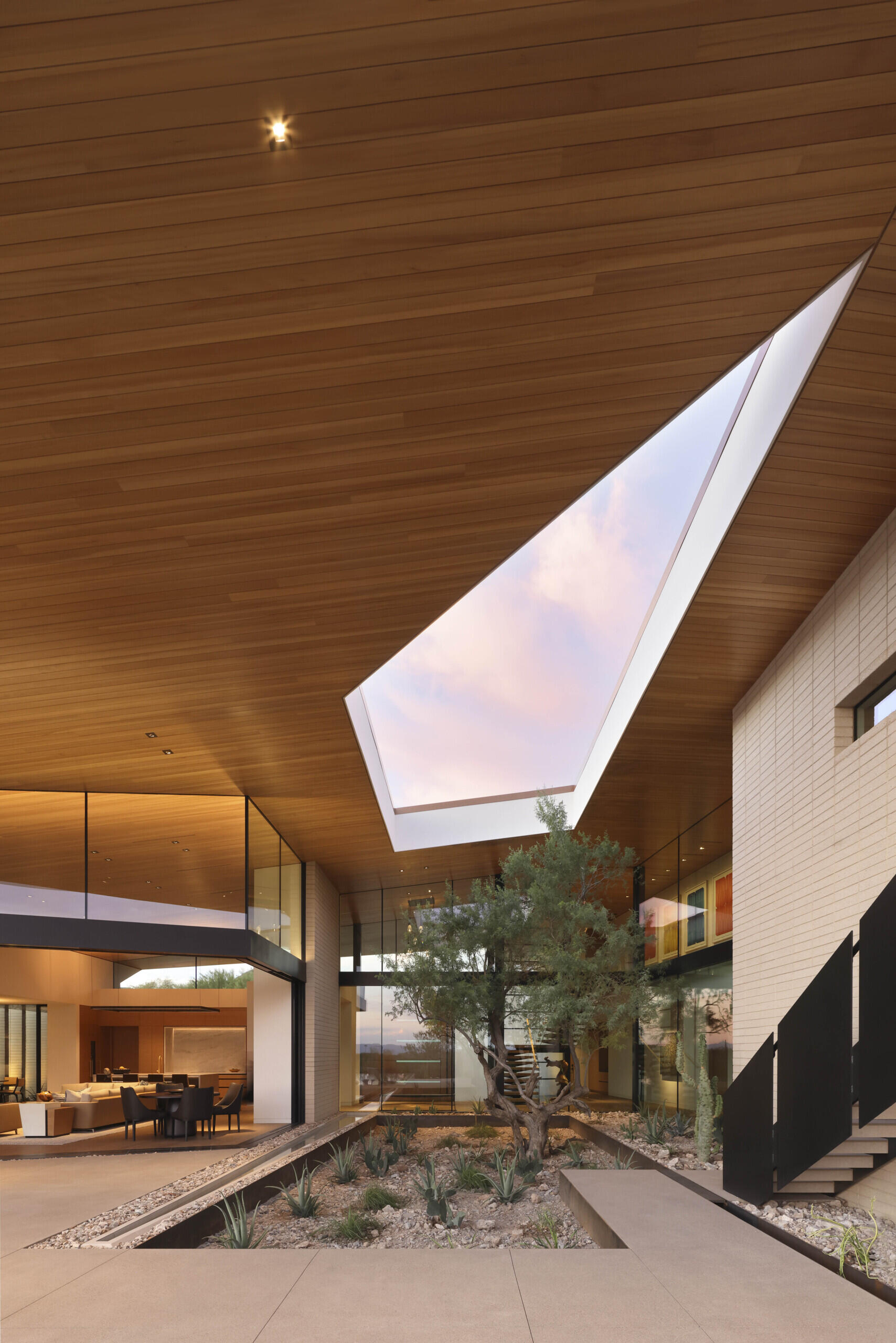 On the southern exposure, glass walls dissolve boundaries between indoors and out. The living spaces open to terraces, revealing a courtyard oasis where basins capture rainwater, sustaining lush greenery amid the arid surroundings.