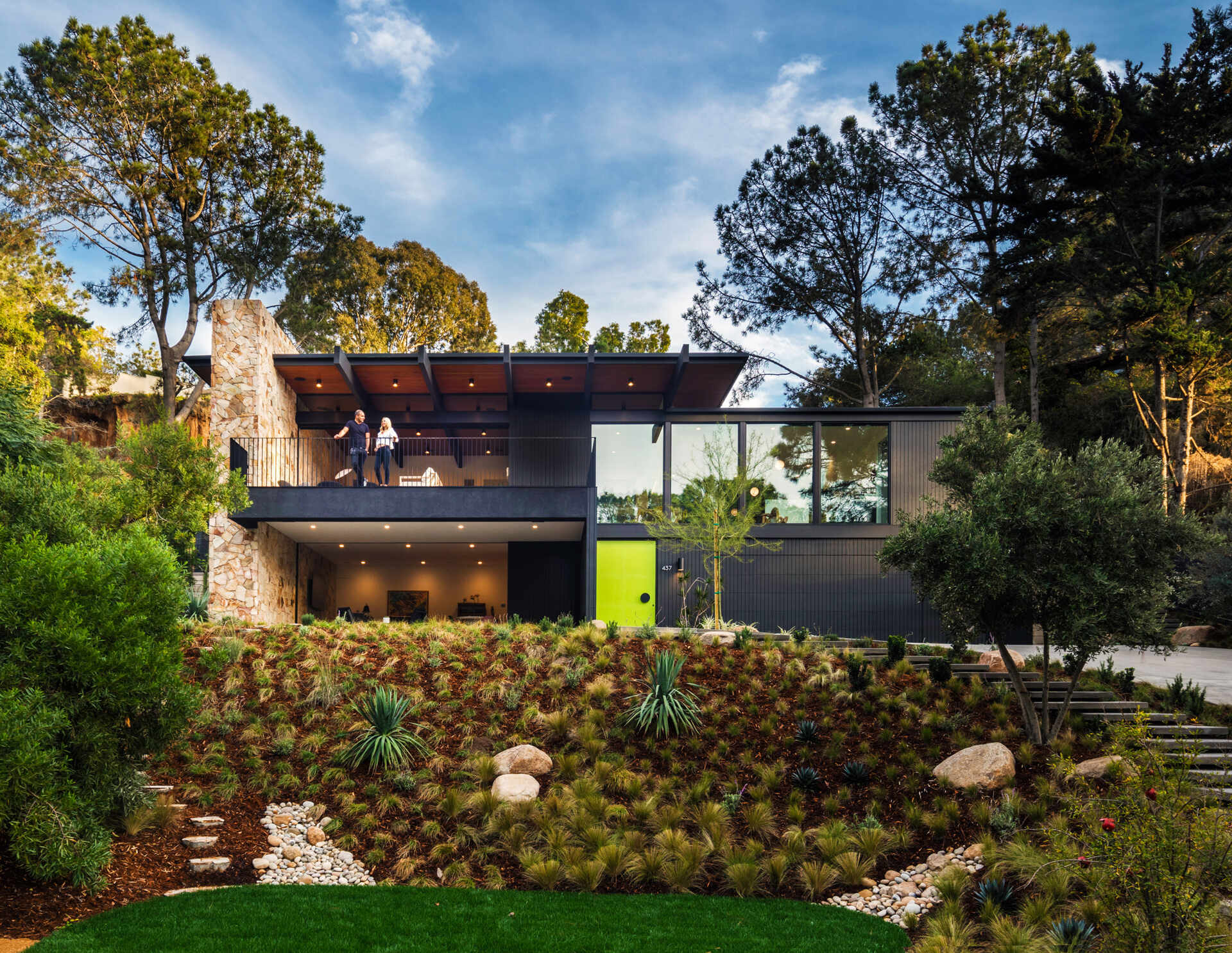 A mid-century modern inspired home with a glass, black, and stone exterior, and a bright oversized front door.