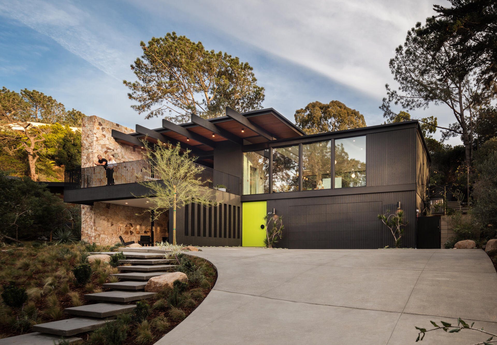 A mid-century modern inspired home with a glass, black, and stone exterior, and a bright oversized front door.