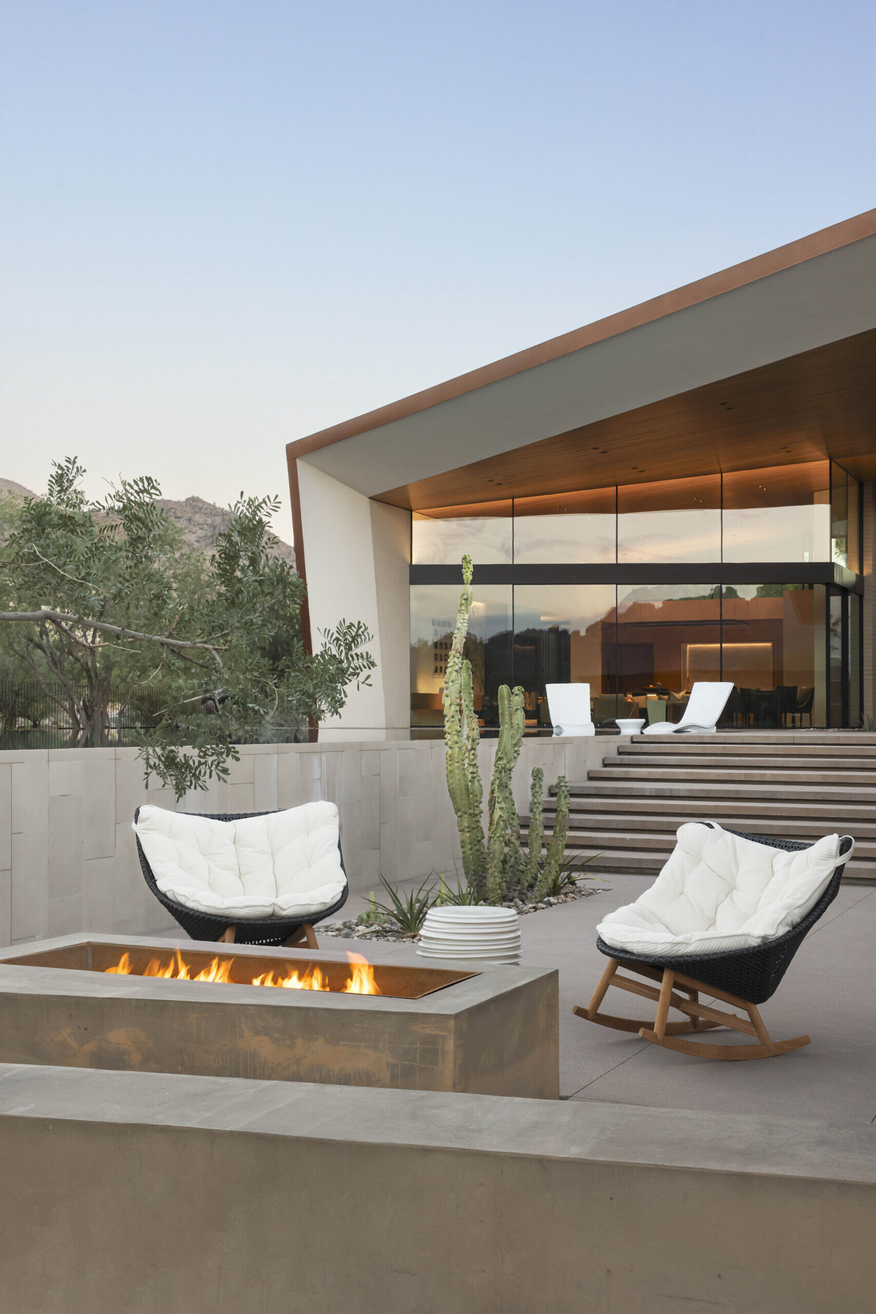 Terraces and balconies offer multiple vantage points to enjoy mountain and city views. A firepit creates a cozy evening gathering space, while an open-air cabana with a patterned metal trellis provides shade among dense vegetation.