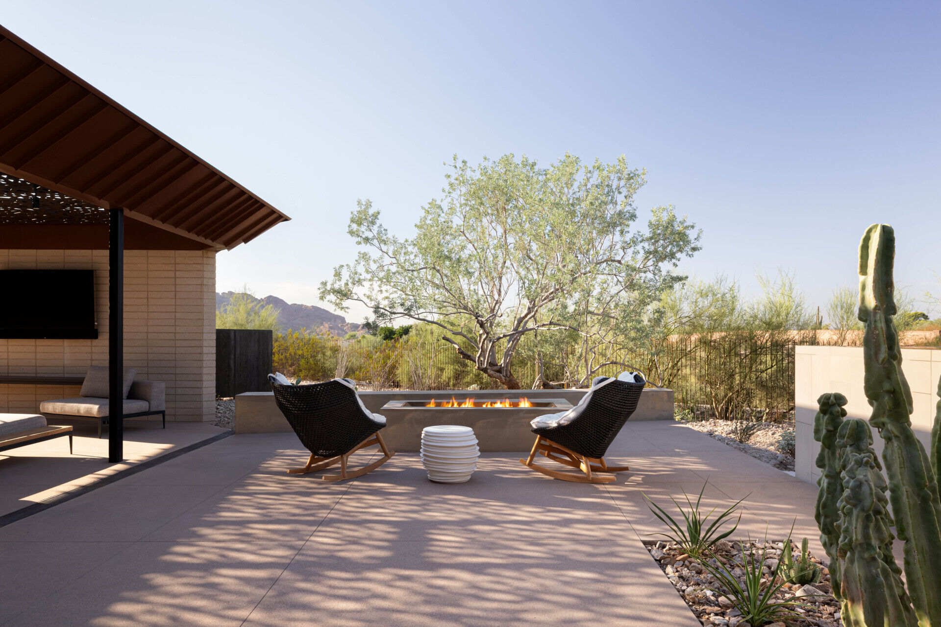 Terraces and balconies offer multiple vantage points to enjoy mountain and city views. A firepit creates a cozy evening gathering space, while an open-air cabana with a patterned metal trellis provides shade among dense vegetation.