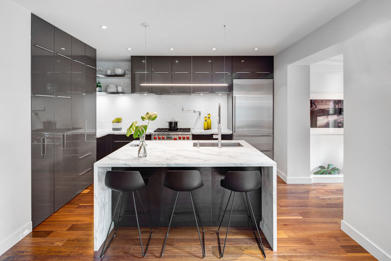 Glossy gray cabinets, a central island, and a custom wine cellar create a contemporary kitchen designed for entertaining.