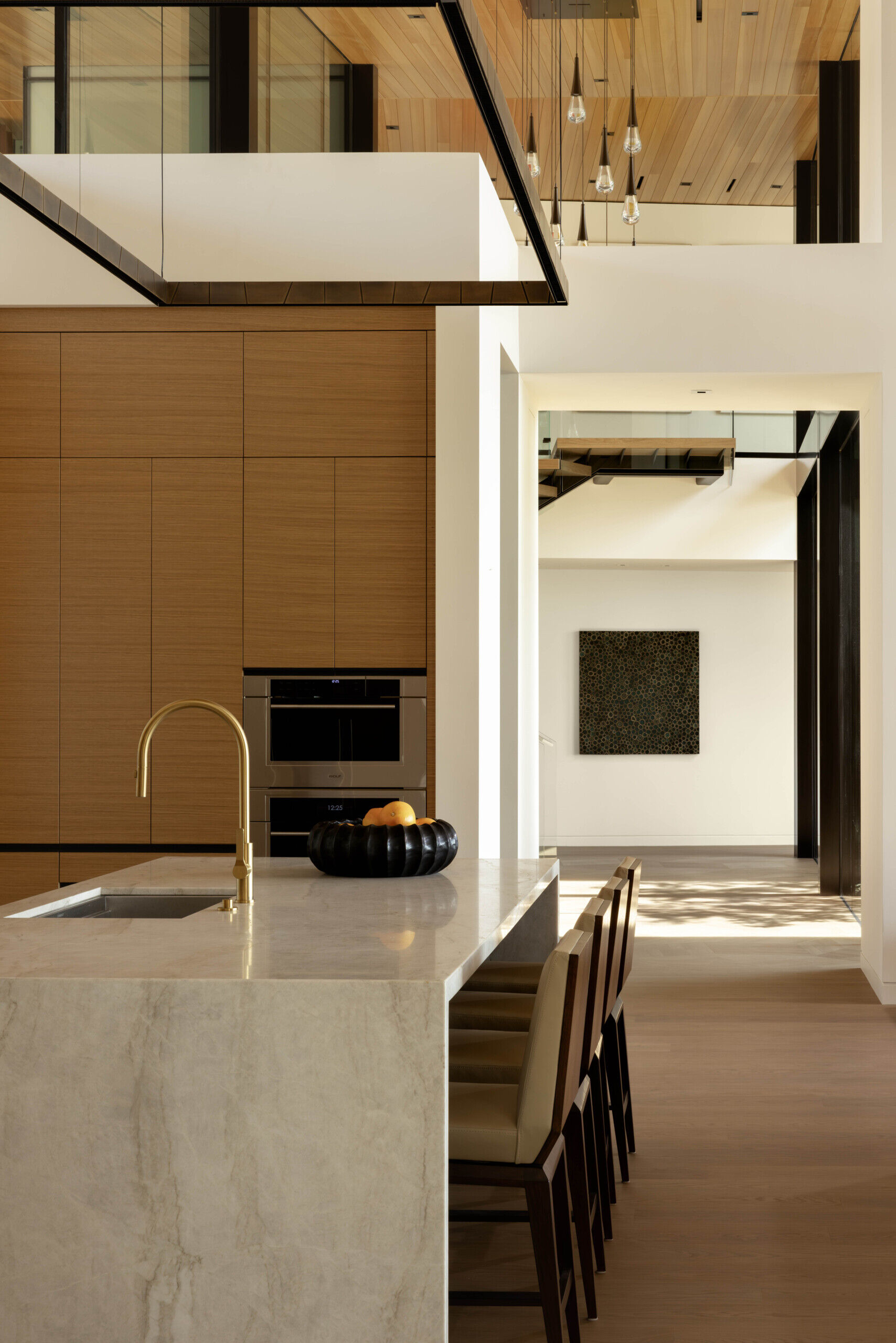 This kitchen continues the home’s natural material palette, combining warm wood tones with refined stone surfaces. Positioned near the open living spaces, it serves as both a functional hub and a visual extension of the design’s elegance.