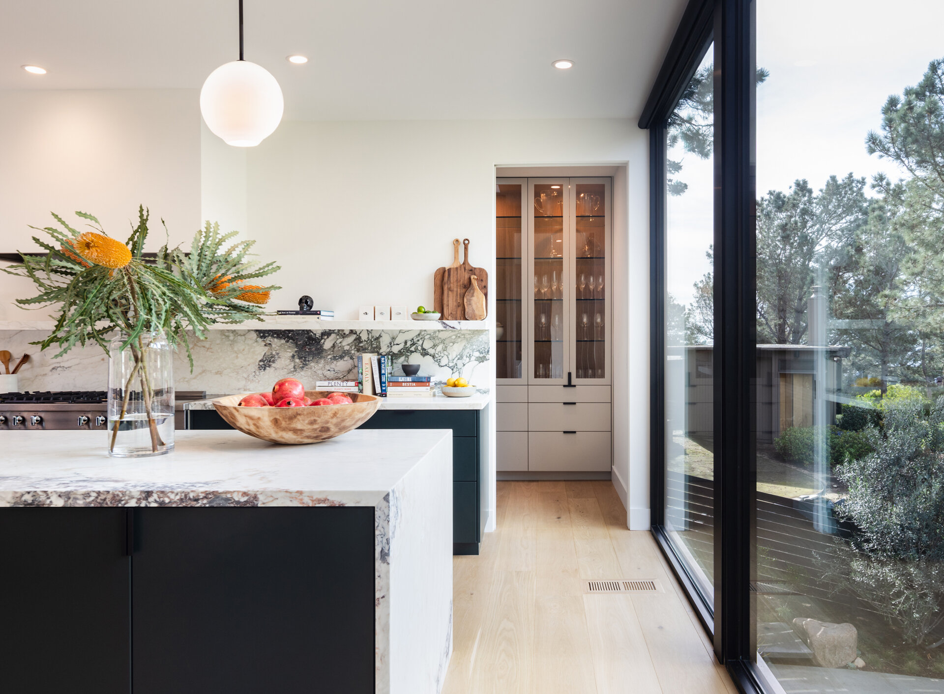 A large marble island defines the kitchen, designed for a family-style approach to cooking and conversation. Black cabinetry provides contrast, while the butler’s pantry provides discreet storage without interrupting the open aesthetic.