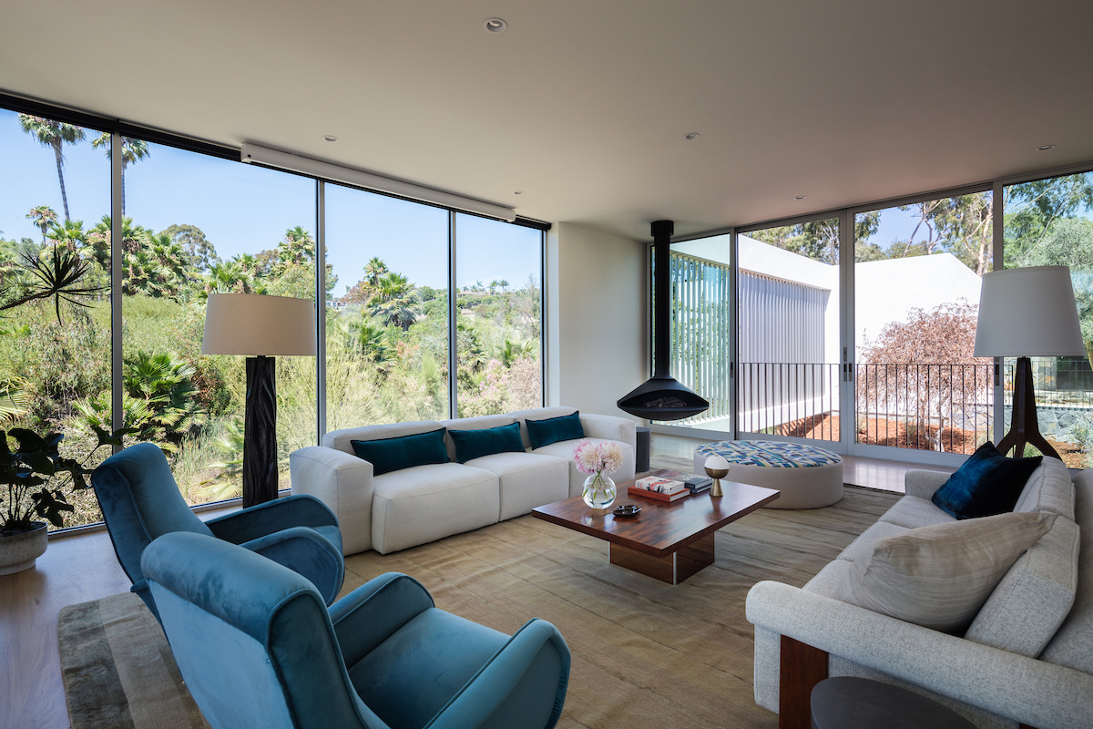 Floor-to-ceiling windows define the living room, flooding the space with natural light and framing views of the grounds and California sunsets. Minimalist details keep the focus on the connection between indoors and outdoors, while a suspended fireplace adds warmth on cool nights.
