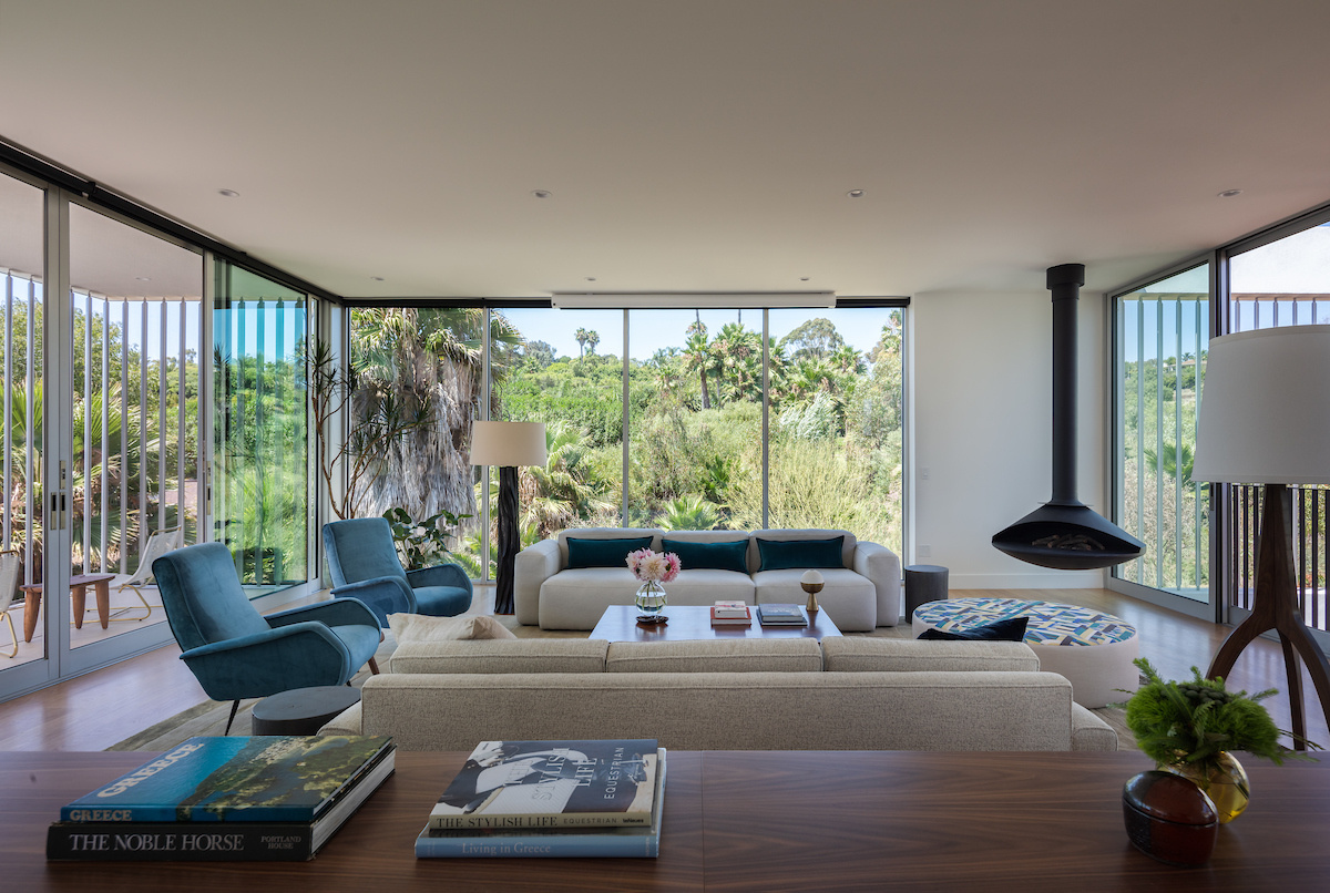 Floor-to-ceiling windows define the living room, flooding the space with natural light and framing views of the grounds and California sunsets. Minimalist details keep the focus on the connection between indoors and outdoors, while a suspended fireplace adds warmth on cool nights.