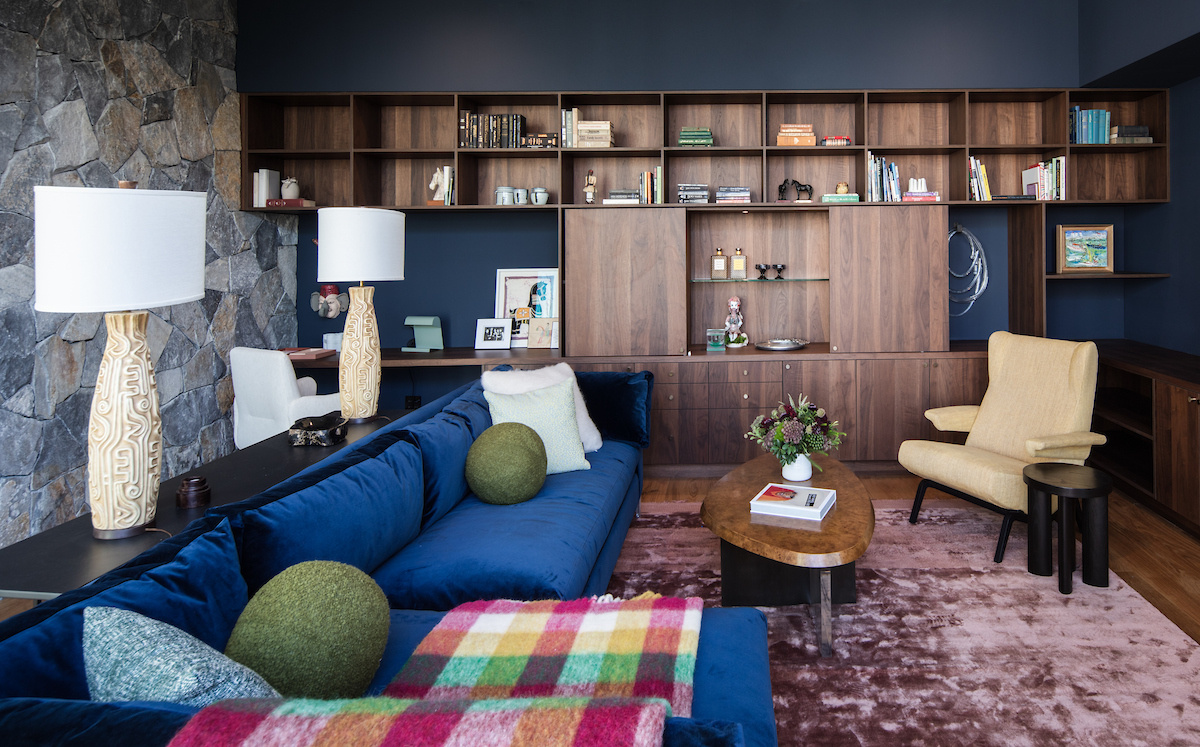 This media room offers a cozy contrast to the open living spaces, designed for comfort while maintaining the modern aesthetic found throughout the home. A wall of custom wood shelving includes a built-in desk, allowing the media room to also act as a home office.