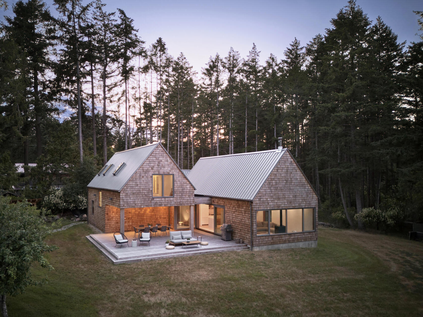 The exterior of this modern cabin is clad in natural cedar shingles, giving the modern form a timeless texture that resonates with the forest surroundings.