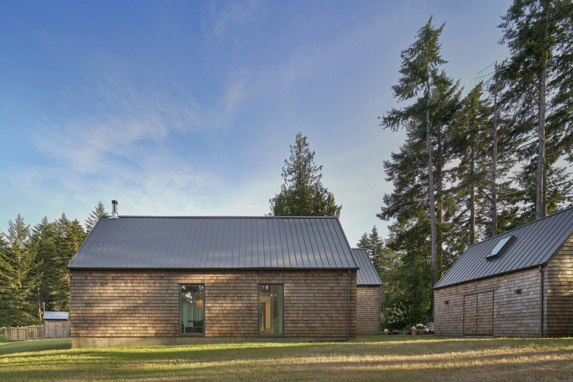 The exterior of this modern cabin is clad in natural cedar shingles, giving the modern form a timeless texture that resonates with the forest surroundings.