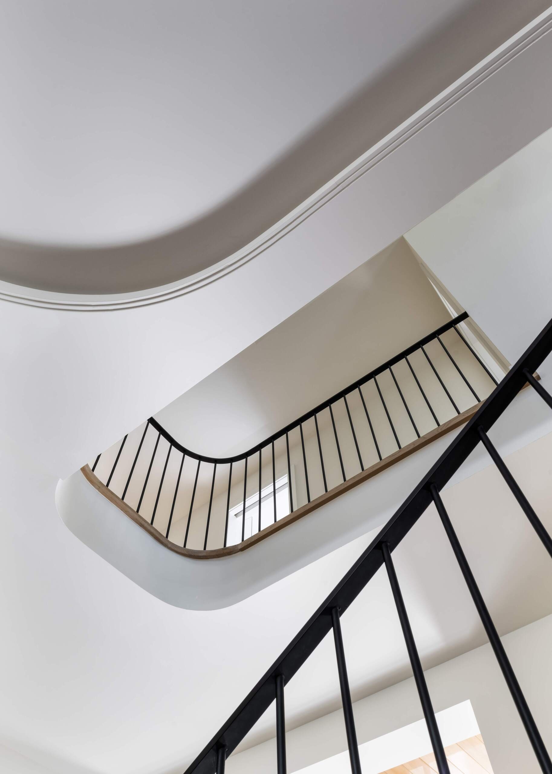 This staircase breaks from convention by not stacking directly between levels. Instead, its discreet placement allows for a more flexible layout. The semi-circular floor opening above gives it presence without overwhelming the interiors.