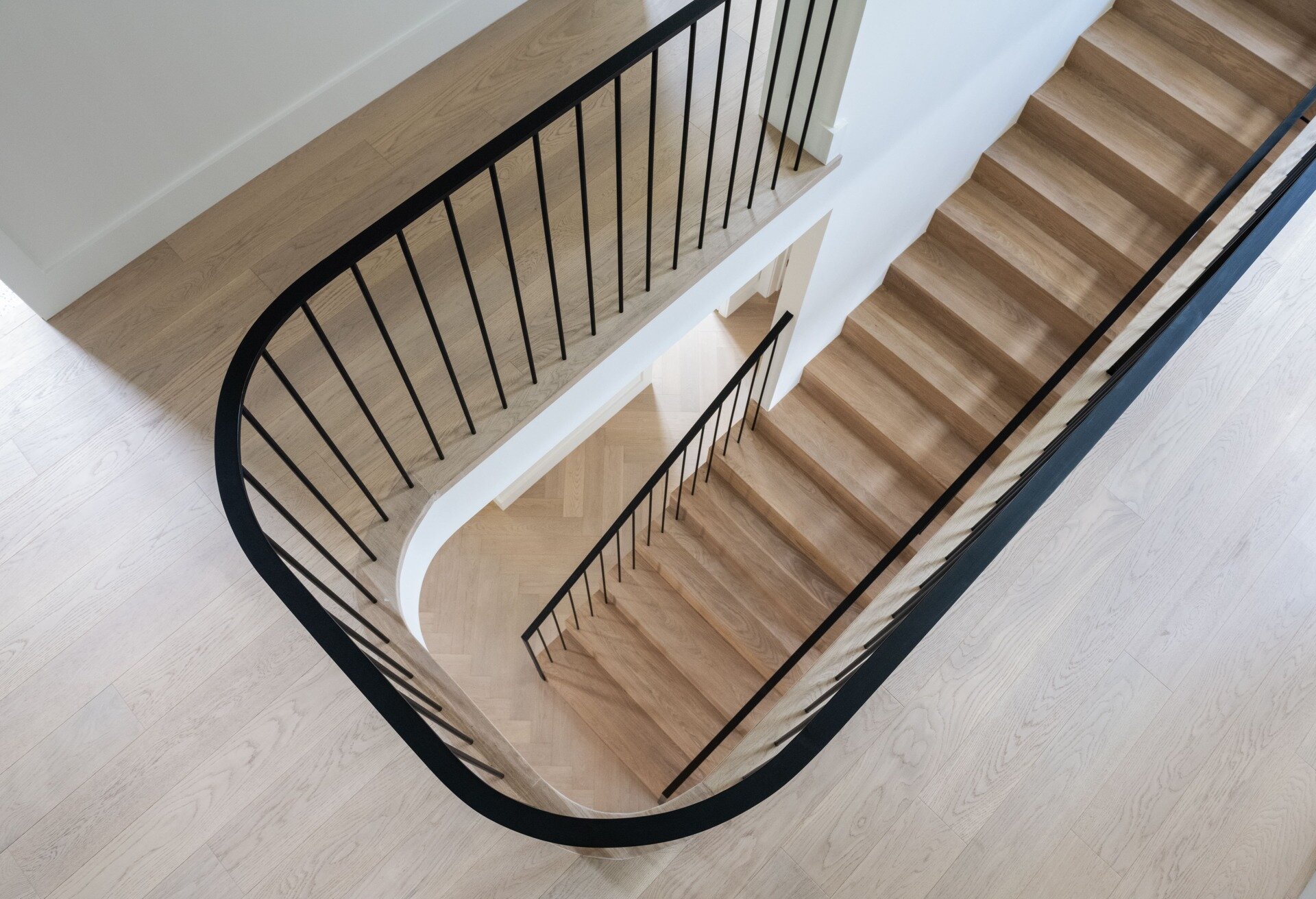 This staircase breaks from convention by not stacking directly between levels. Instead, its discreet placement allows for a more flexible layout. The semi-circular floor opening above gives it presence without overwhelming the interiors.