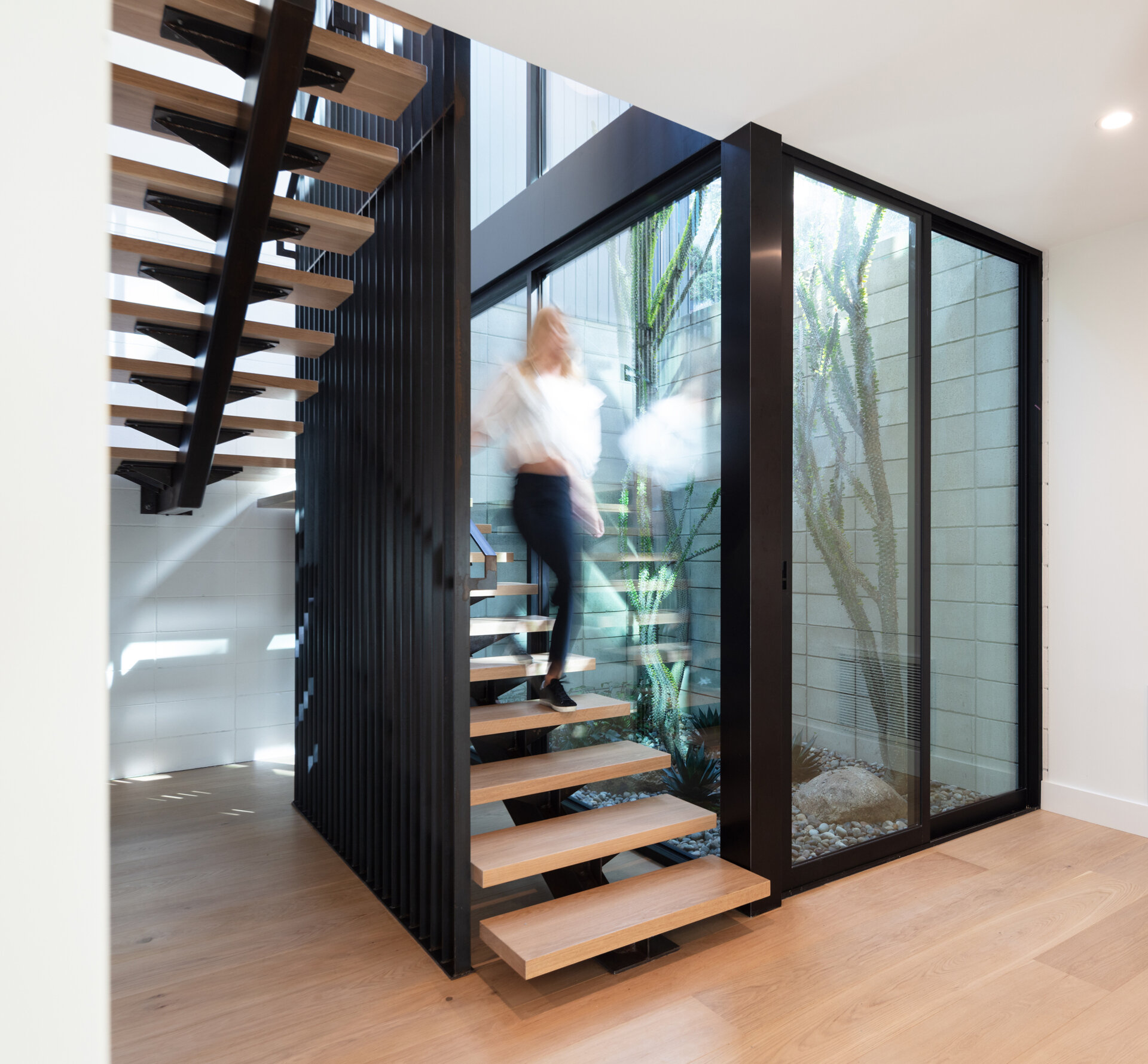 Modern wood and steel stairs are next to an atrium with plants.