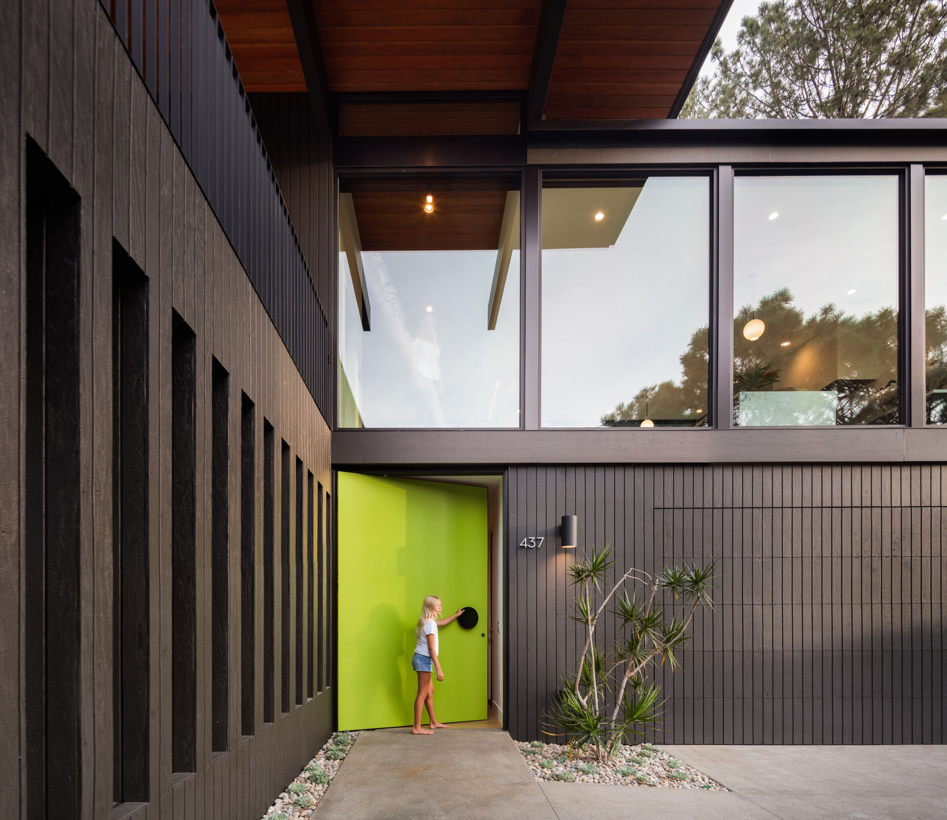 A mid-century modern inspired home with a glass, black, and stone exterior, and a bright oversized front door.