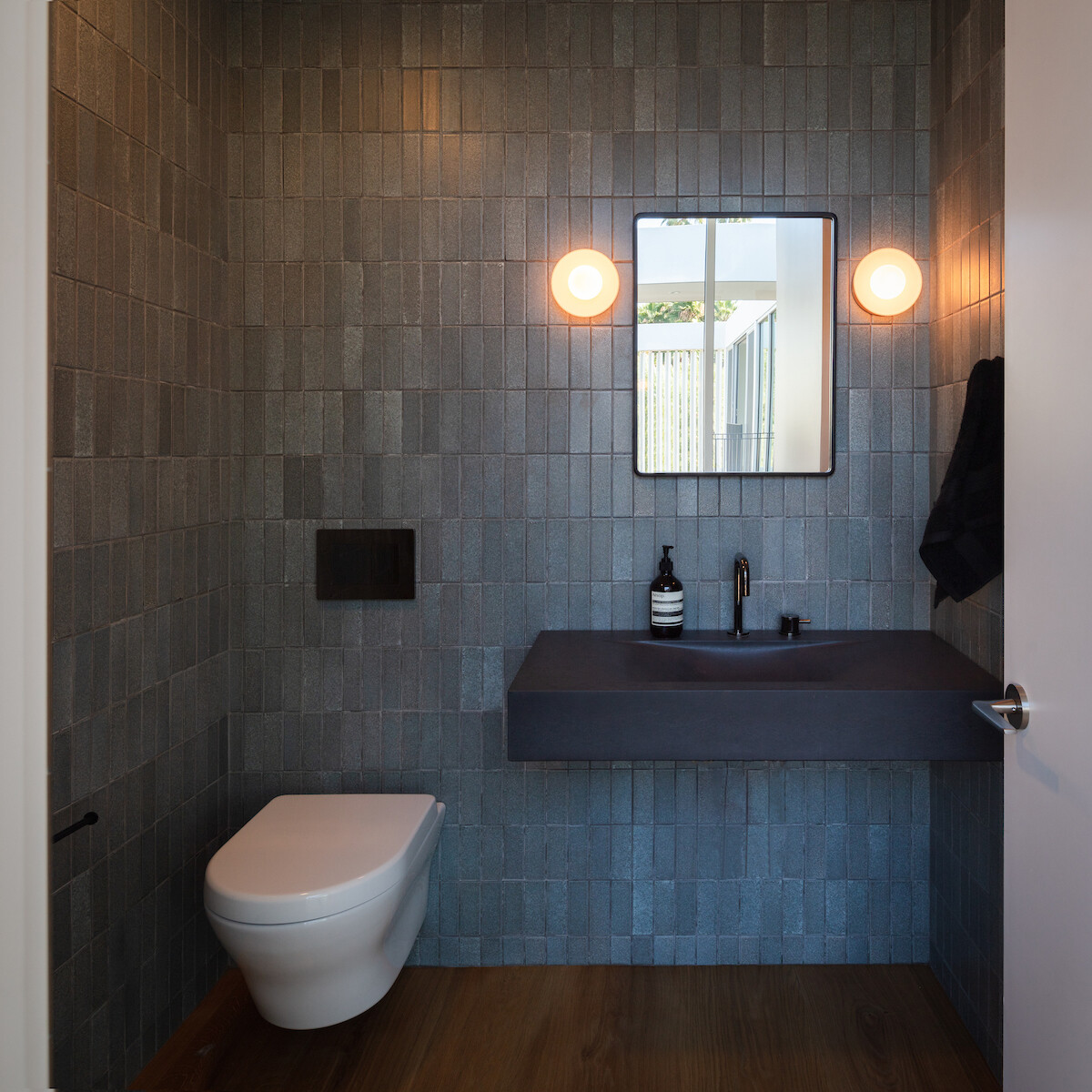 In this powder room, vertical tiles in a matte dark finish cover the walls, while a floating matte black sink adds a sculptural touch. 
