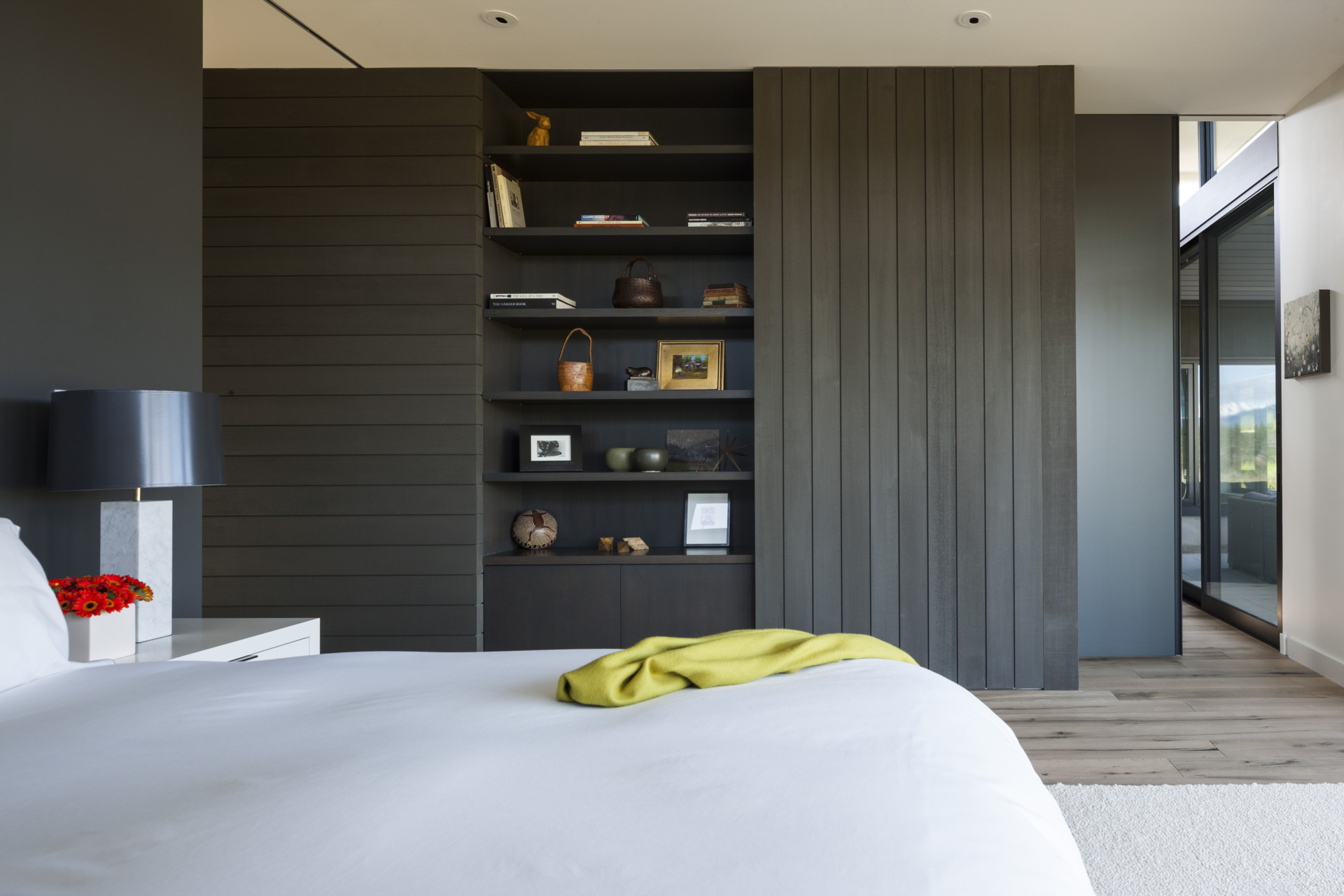 Wrapped in windows, this bedroom wakes to mountain views. Soft white walls and bedding keep the palette quiet, while a mossy green throw adds a relaxed hit of color and a mid-century chair with graphic upholstery creates character without clutter.