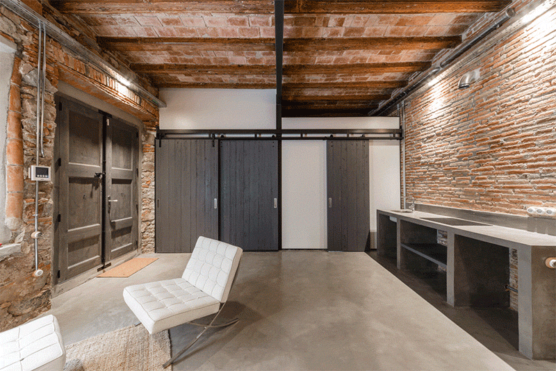 A guest suite in Barcelona that doubles as a studio, featuring exposed stone walls, a polished concrete floor, and flexible barn doors.
