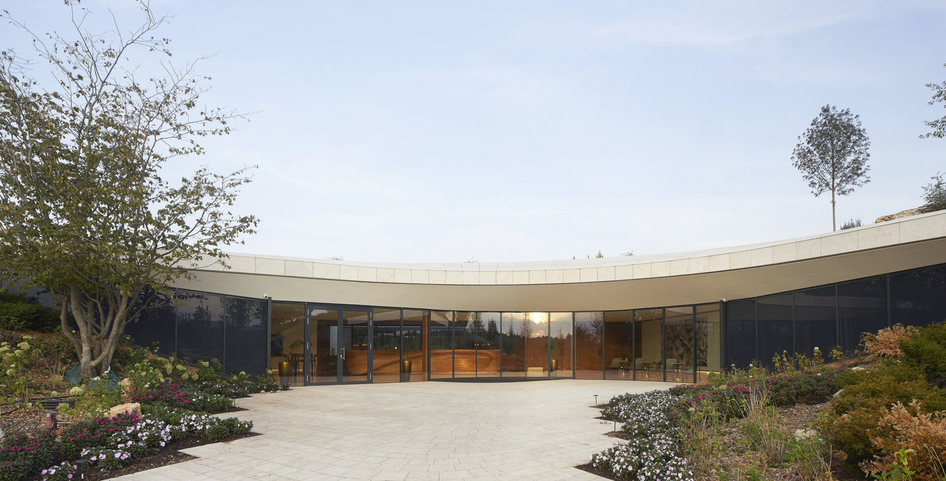 The curved glass entrance and skylit lobby guide visitors inward, framing vineyard views and creating a warm, welcoming transition from outdoors to interior.