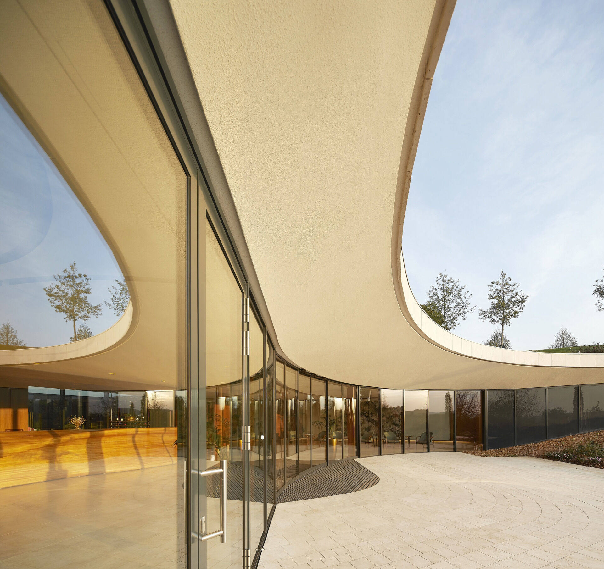The curved glass entrance and skylit lobby guide visitors inward, framing vineyard views and creating a warm, welcoming transition from outdoors to interior.