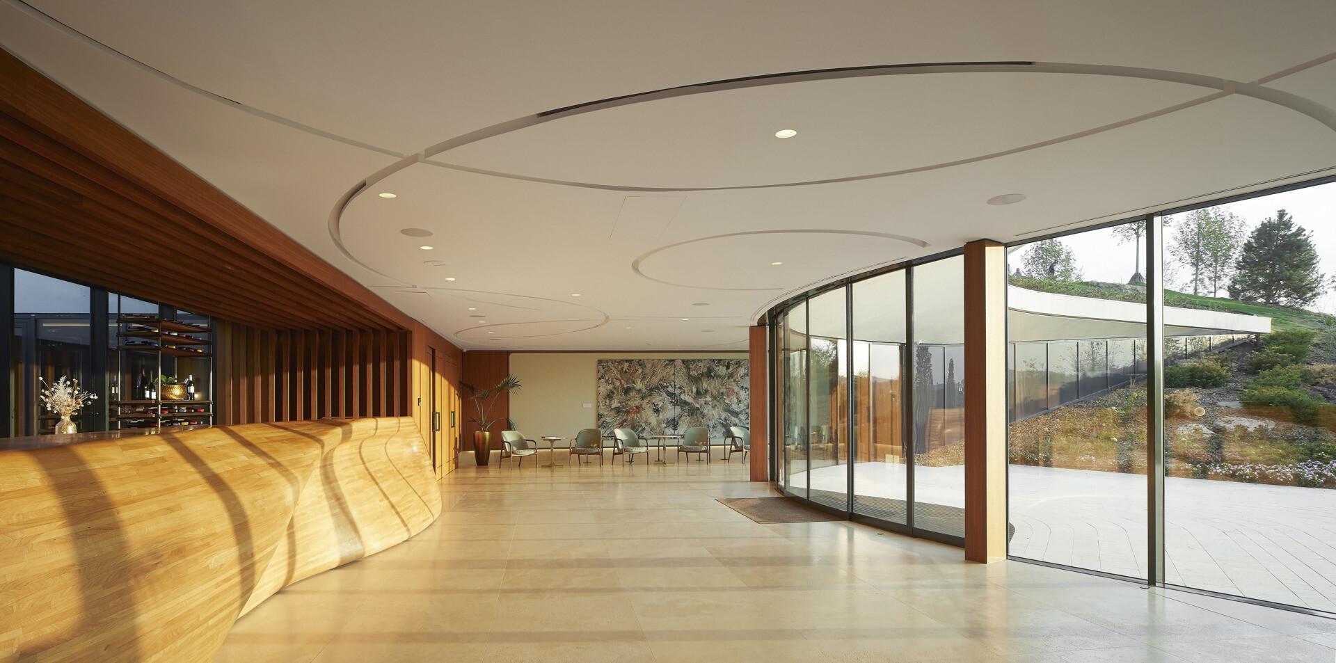 The curved glass entrance and skylit lobby guide visitors inward, framing vineyard views and creating a warm, welcoming transition from outdoors to interior.