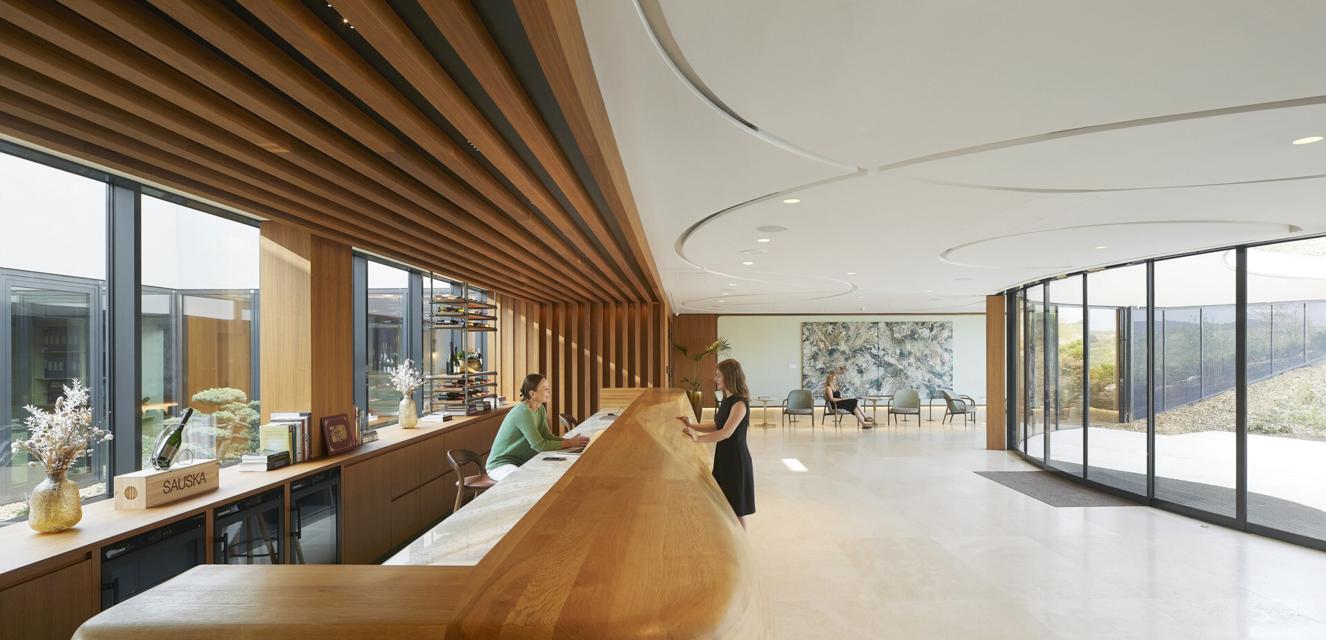 The curved glass entrance and skylit lobby guide visitors inward, framing vineyard views and creating a warm, welcoming transition from outdoors to interior.