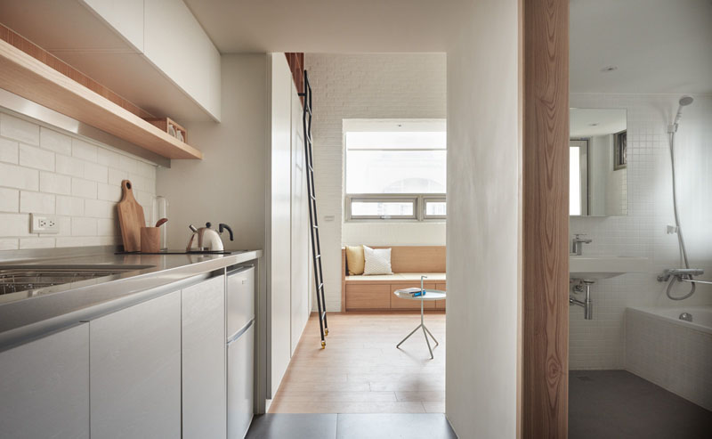 Upon entering, this loft apartment opens into a narrow hallway. To the left, a cleverly arranged kitchen features a small cooktop, mini-fridge, washer/dryer, and essential storage, making it practical without crowding the space.
