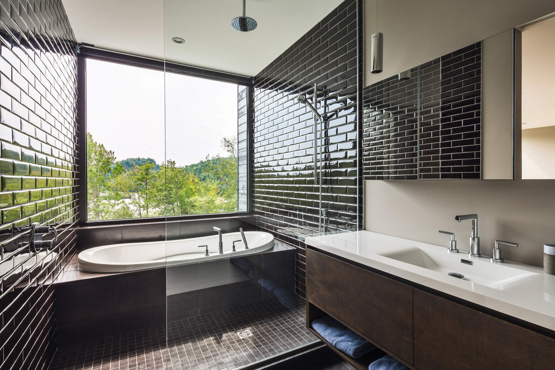 A glass-partitioned ensuite with black tile and natural views combines elegance with calm.