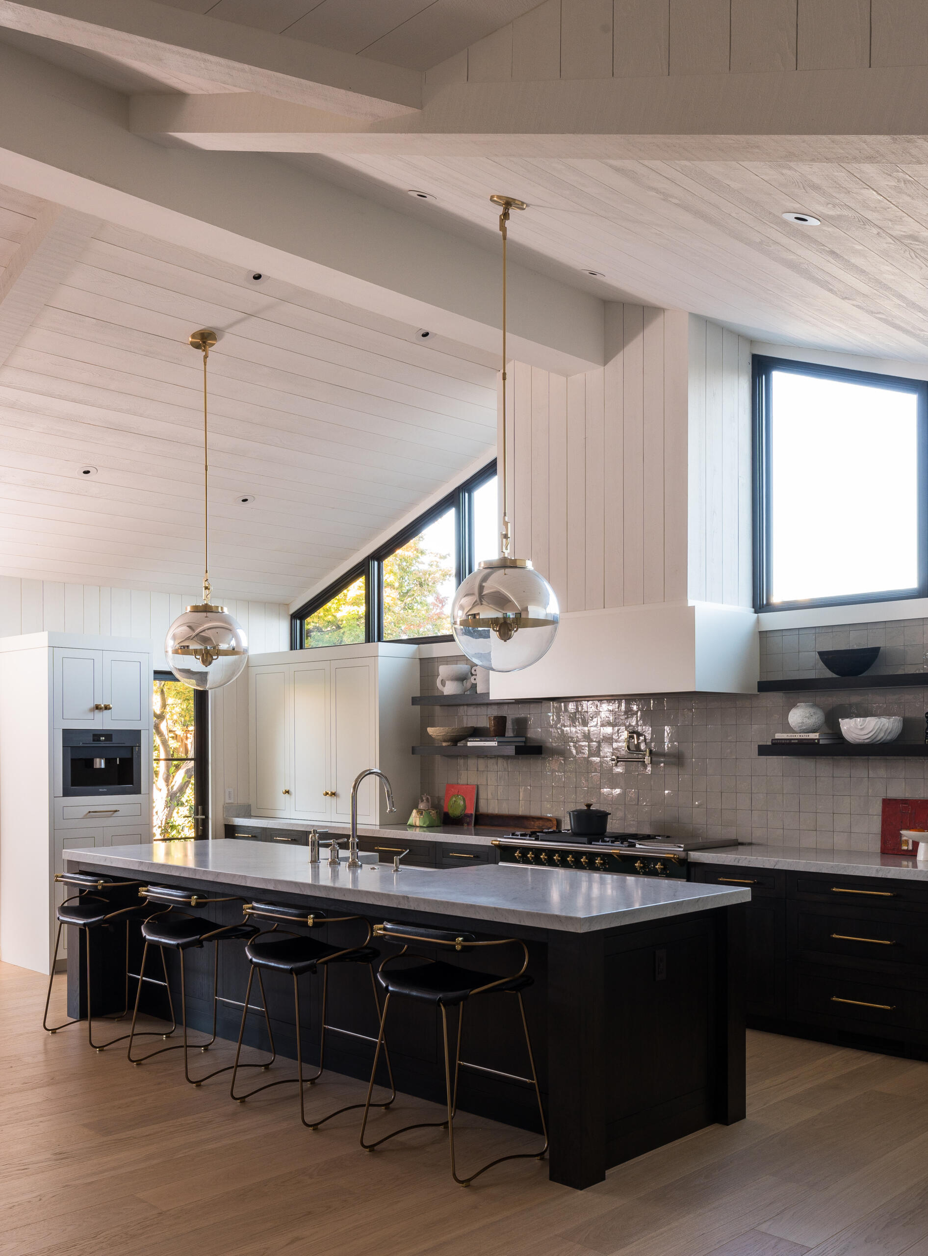 In this contemporary kitchen, triangular windows draw in both sunlight and landscape views, creating a distinctive connection between daily routines and the beauty outside. Together, the kitchen and dining spaces embody the remodel’s central vision: openness, light, and a harmonious relationship with the outdoors.