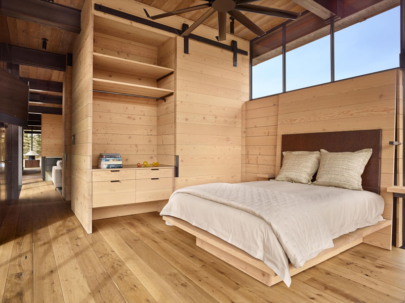 The bedroom of this modern industrial house blends warm wood finishes with industrial details like a sliding barn door and steel ceiling fan.