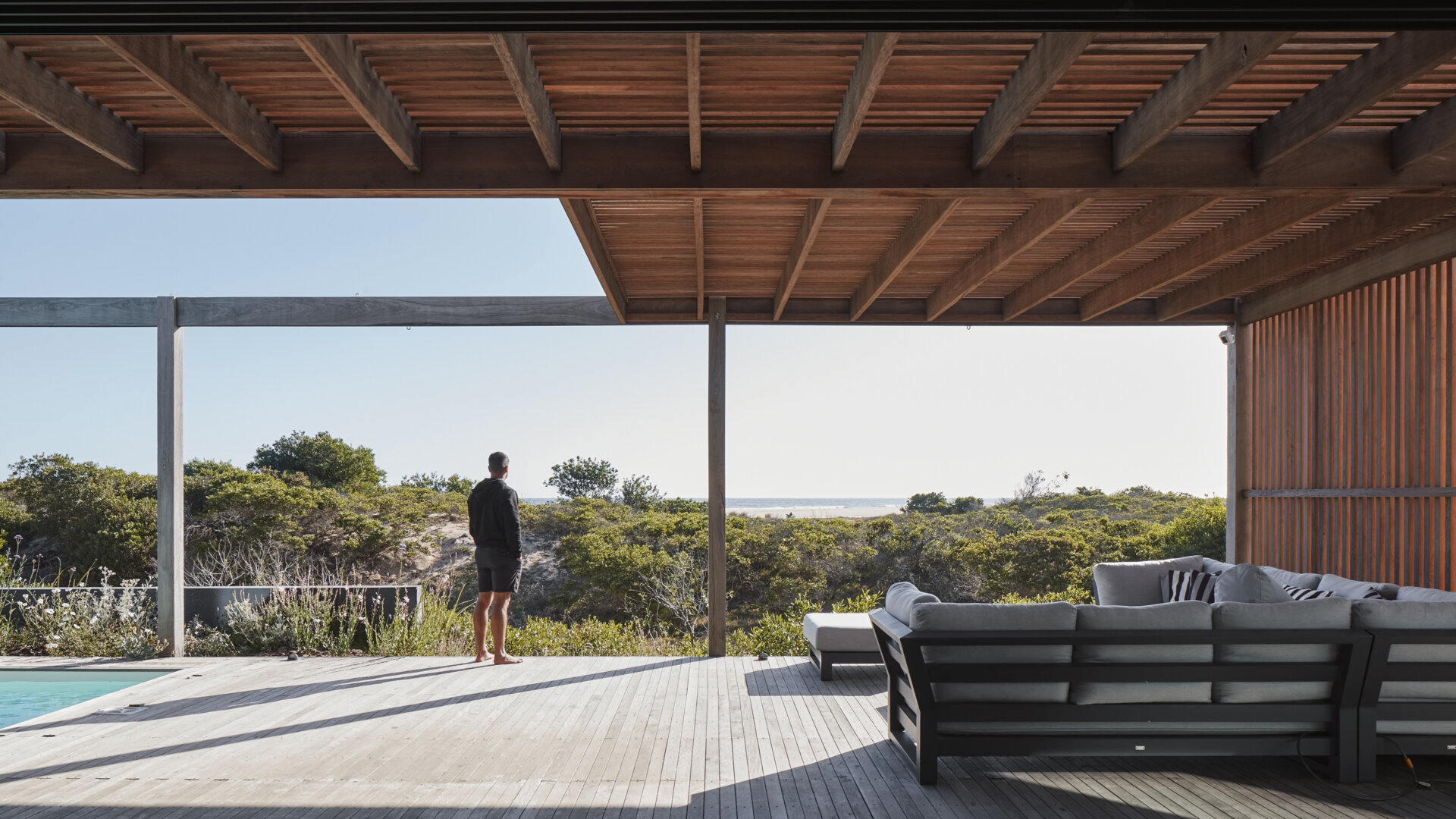 This prefabricated modular house, clad in wood, has a swimming pool, and preserves the sandy terrain while opening all rooms toward the sea.