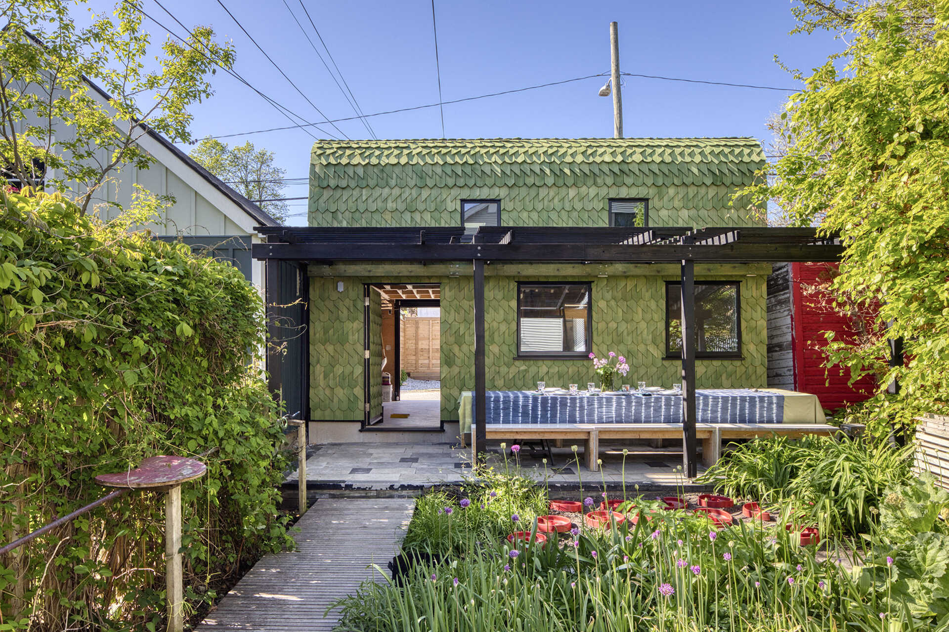 A Toronto laneway garage transformed into The Dragon, bold, playful, and full of architectural charm. It has a pergola and is covered in cedar shingles with a green pine tar finish.