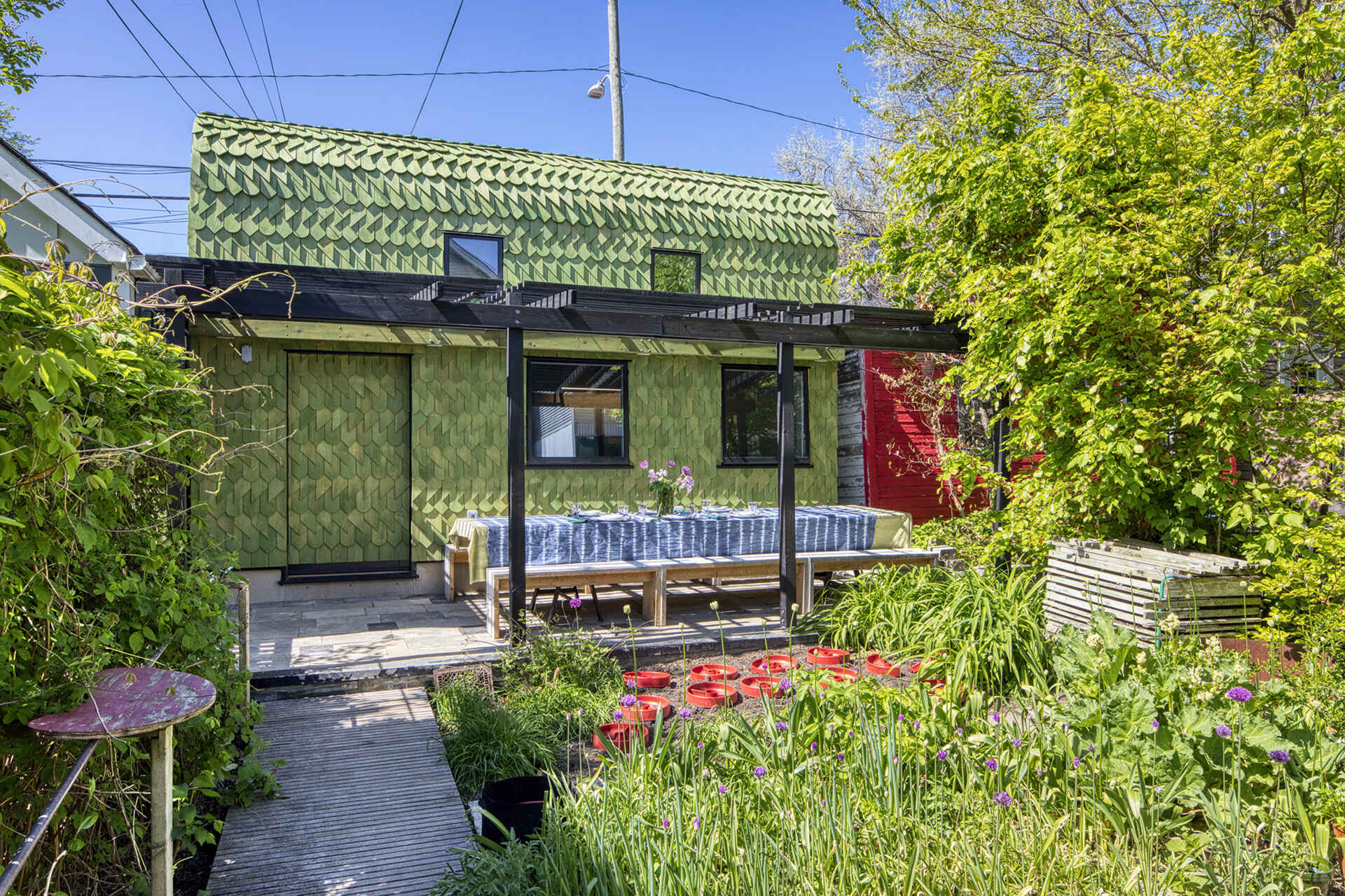 A Toronto laneway garage transformed into The Dragon, bold, playful, and full of architectural charm. It has a pergola and is covered in cedar shingles with a green pine tar finish.
