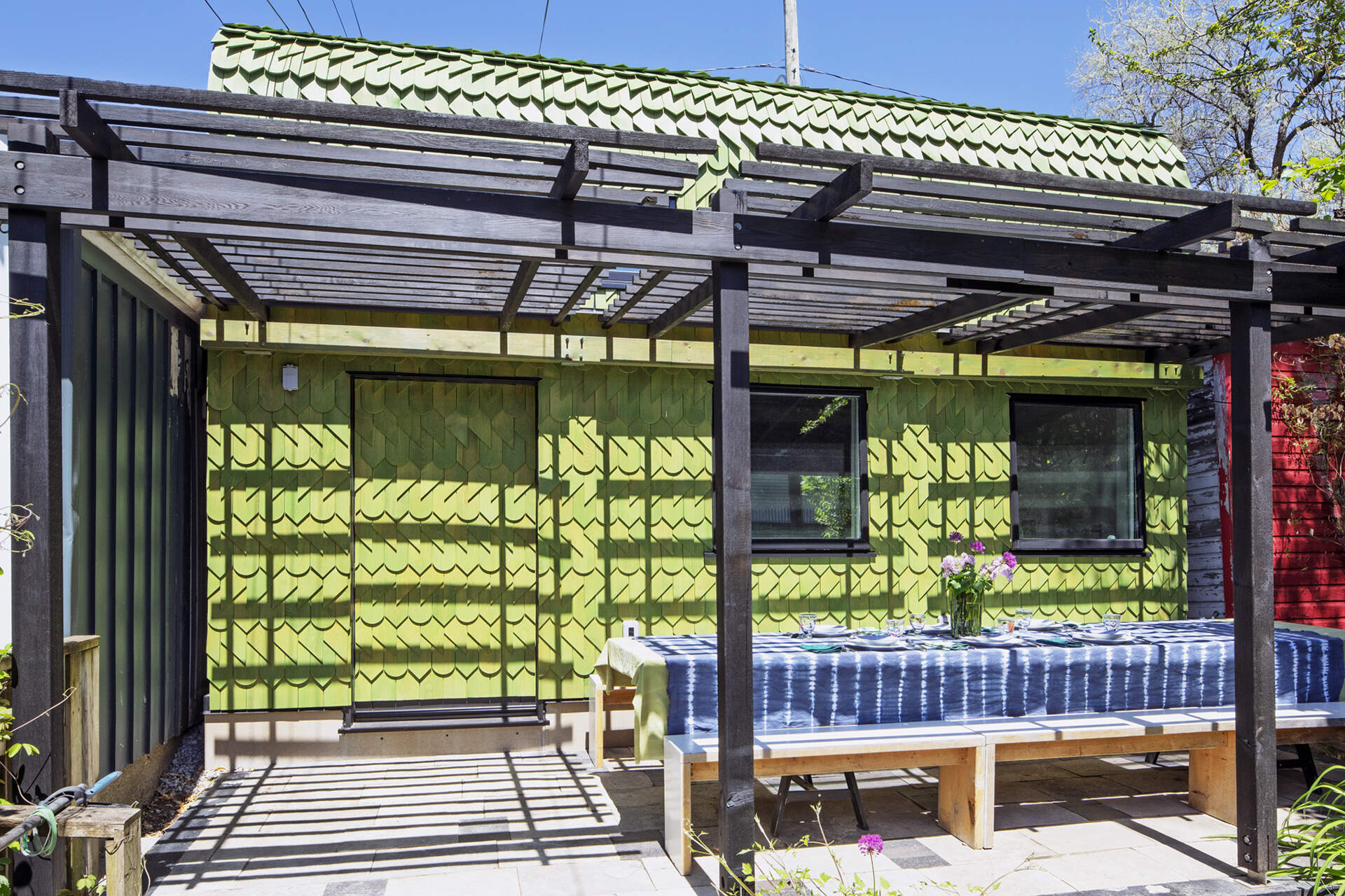 A Toronto laneway garage transformed into The Dragon, bold, playful, and full of architectural charm. It has a pergola and is covered in cedar shingles with a green pine tar finish.