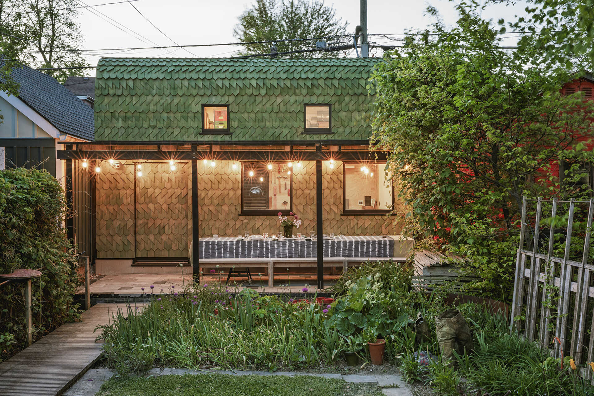 A Toronto laneway garage transformed into The Dragon, bold, playful, and full of architectural charm. It has a pergola and is covered in cedar shingles with a green pine tar finish.