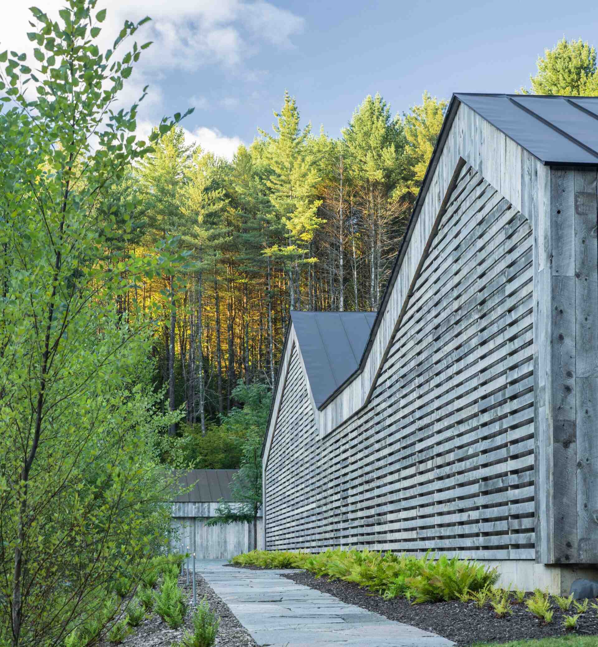 A Vermont guest house takes its shape from the classic woodshed, with gabled roofs that reimagine a familiar rural form. The house is clad in reclaimed snow fencing, weathered boards that give the structure instant character and texture.