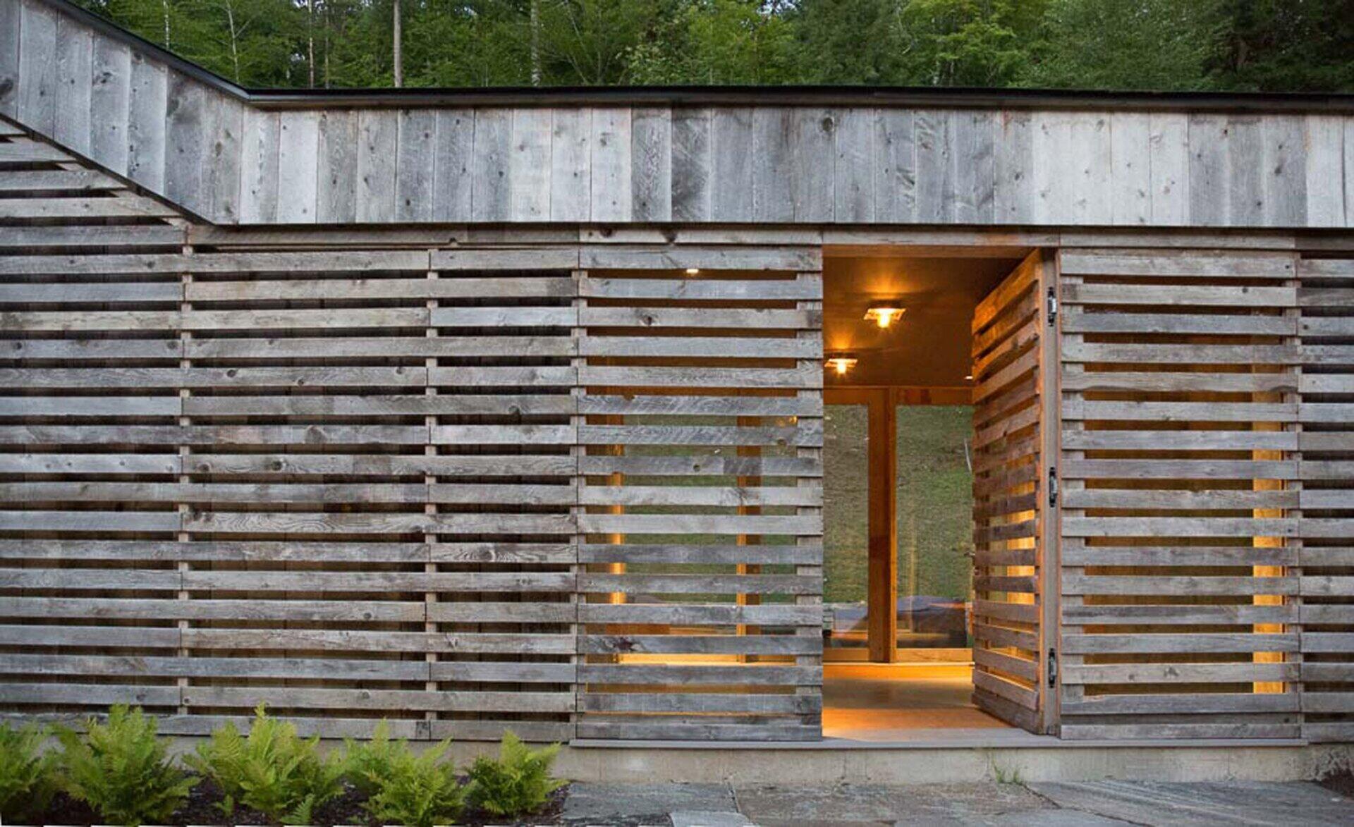 A Vermont guest house takes its shape from the classic woodshed, with gabled roofs that reimagine a familiar rural form. The house is clad in reclaimed snow fencing, weathered boards that give the structure instant character and texture.