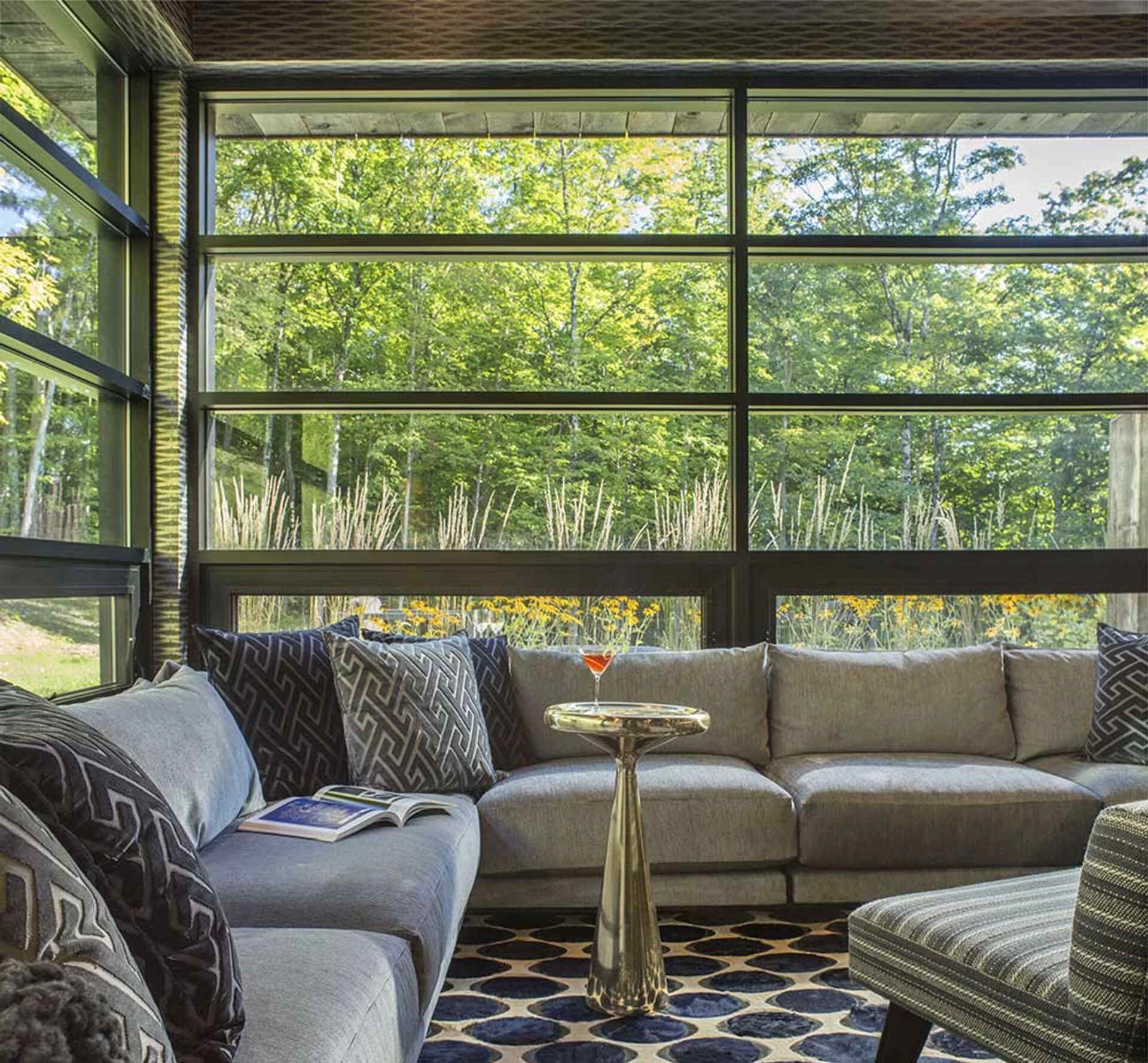 This cozy living room wraps around a corner sofa, with black-framed windows that pull in daylight and forest views.