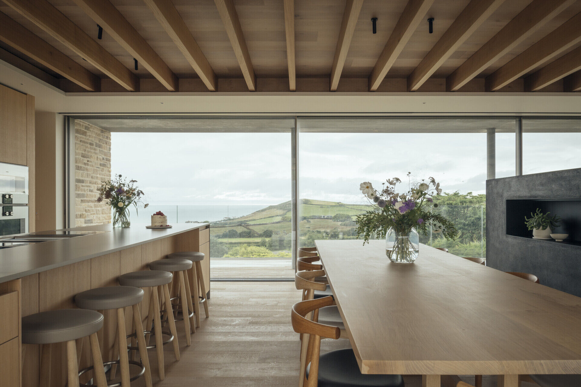 Set within the open plan, the dining area enjoys the same expansive views and light. Its placement creates a natural flow between kitchen and living, with glazed doors that open onto outdoor terraces, making it ideal for family gatherings and shared meals.