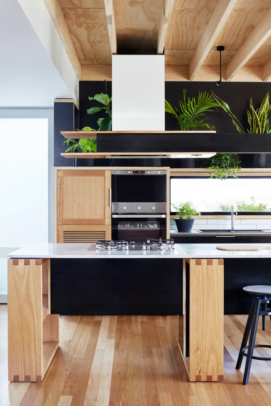The kitchen and dining areas sit side by side, designed to feel both functional and welcoming. The kitchen pairs black formply drawer fronts with pale wood, striking a balance between boldness and warmth. A row of greenery perched above the cabinetry softens the space, adding life and texture.