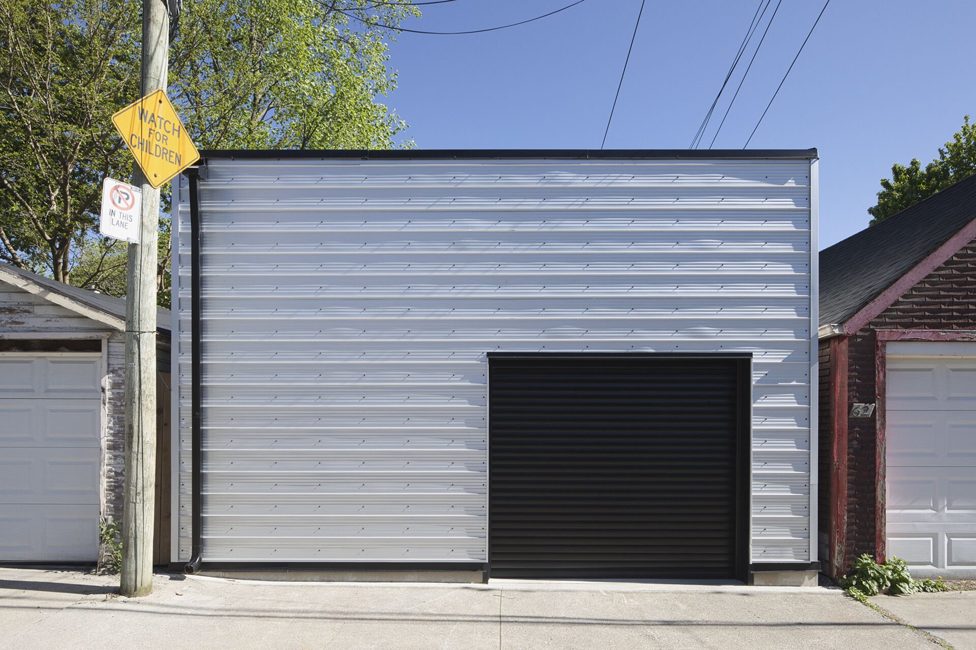 A laneway garage with metal siding and a sleek black aluminum roll-up door.