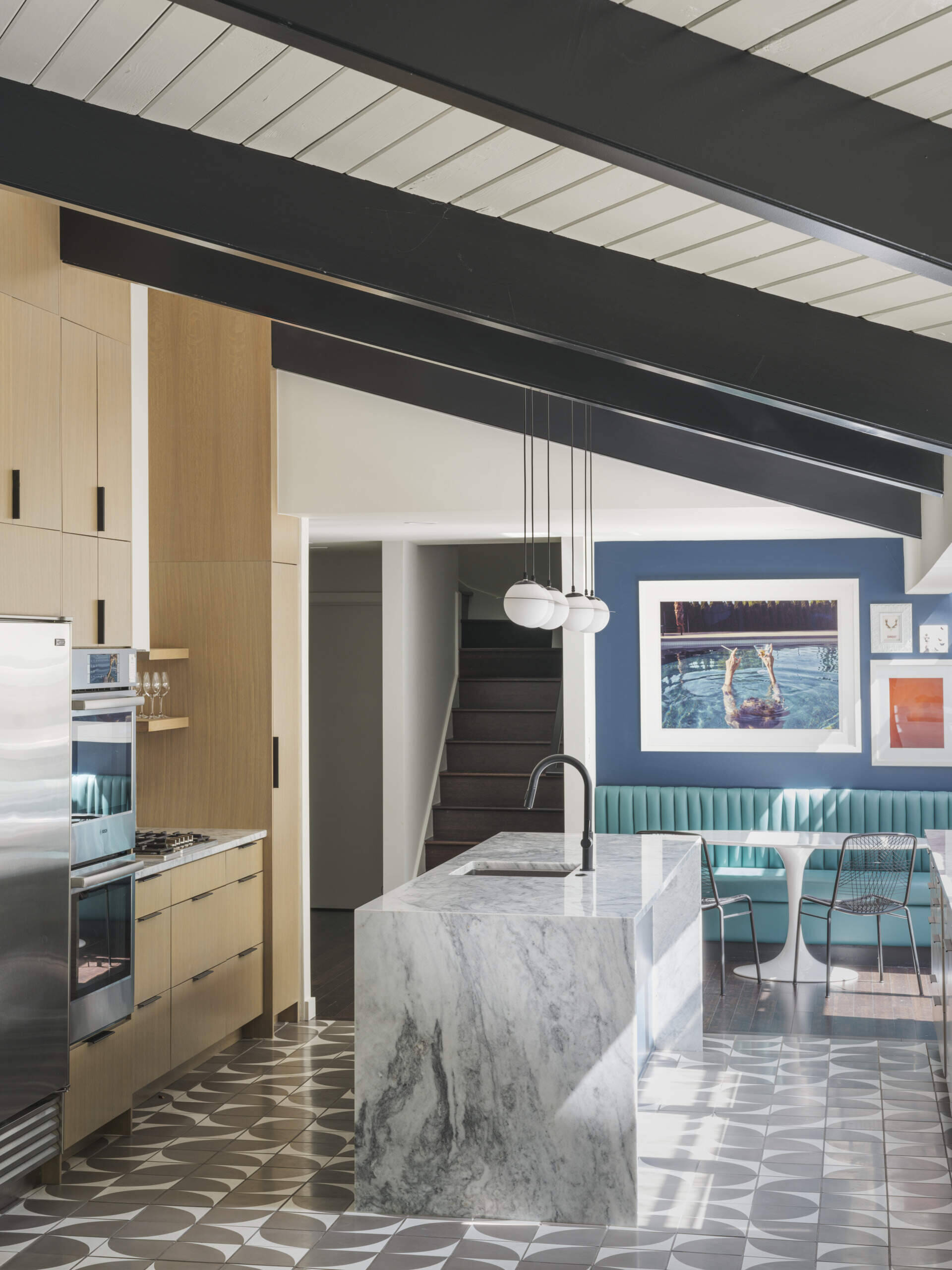 What was once walled-off is now the heart of the house. The new kitchen opens fully to the lounge and living room with a generous island at its center. Oak veneer cabinetry, stone counters, and Cle tile floors strike a balance between mid-century simplicity and modern function. 
