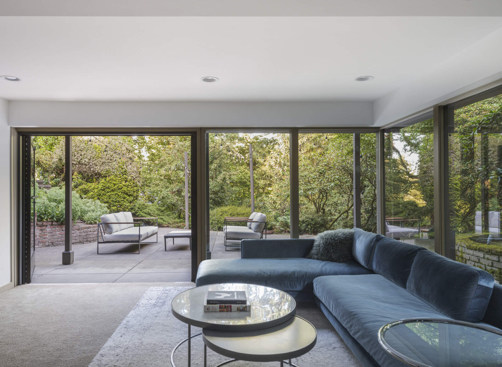A modern living room with floor-to-ceiling windows and doors that open to a patio.