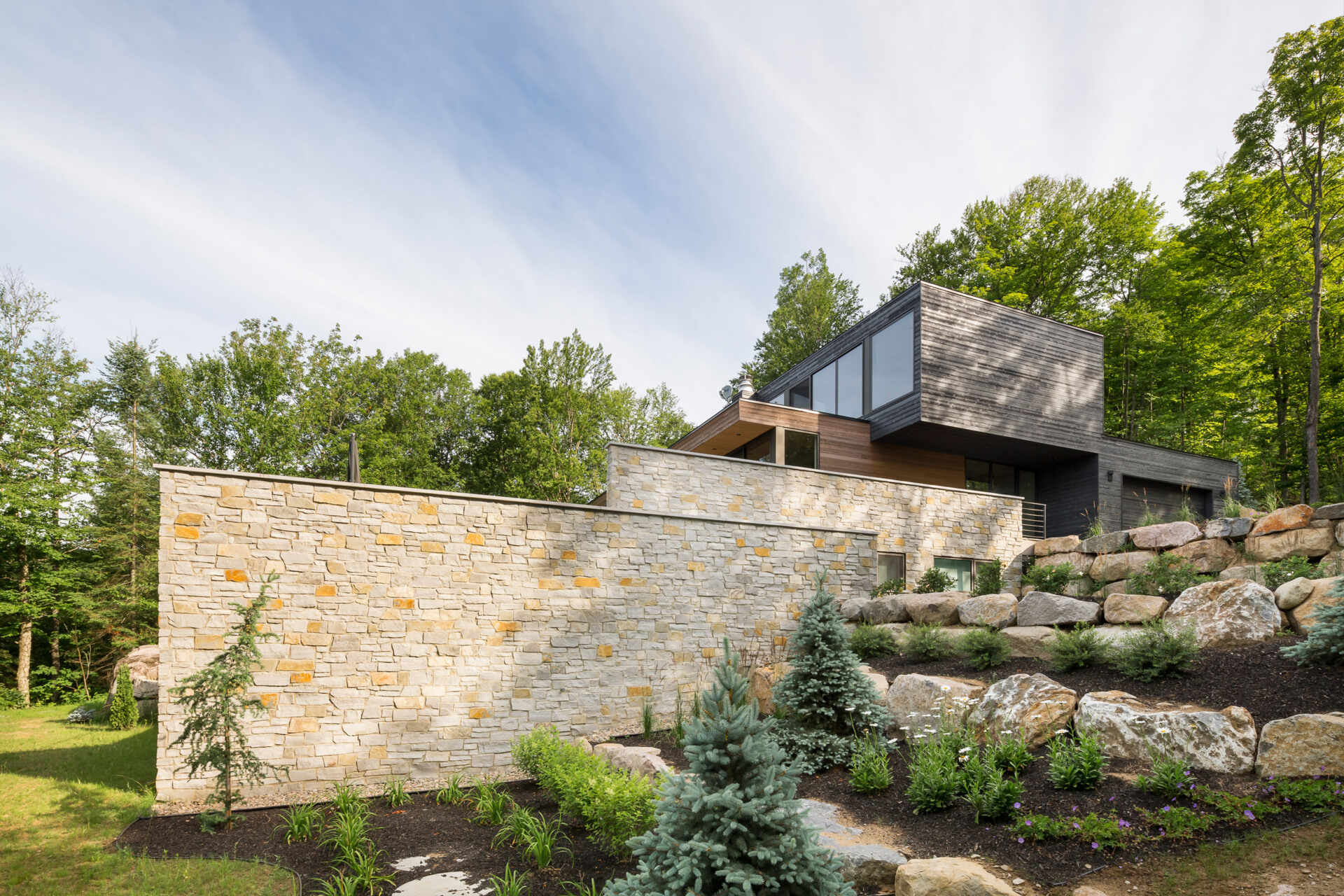 Terraced outdoor spaces framed by natural stone walls blend this modern home seamlessly into its rocky setting.