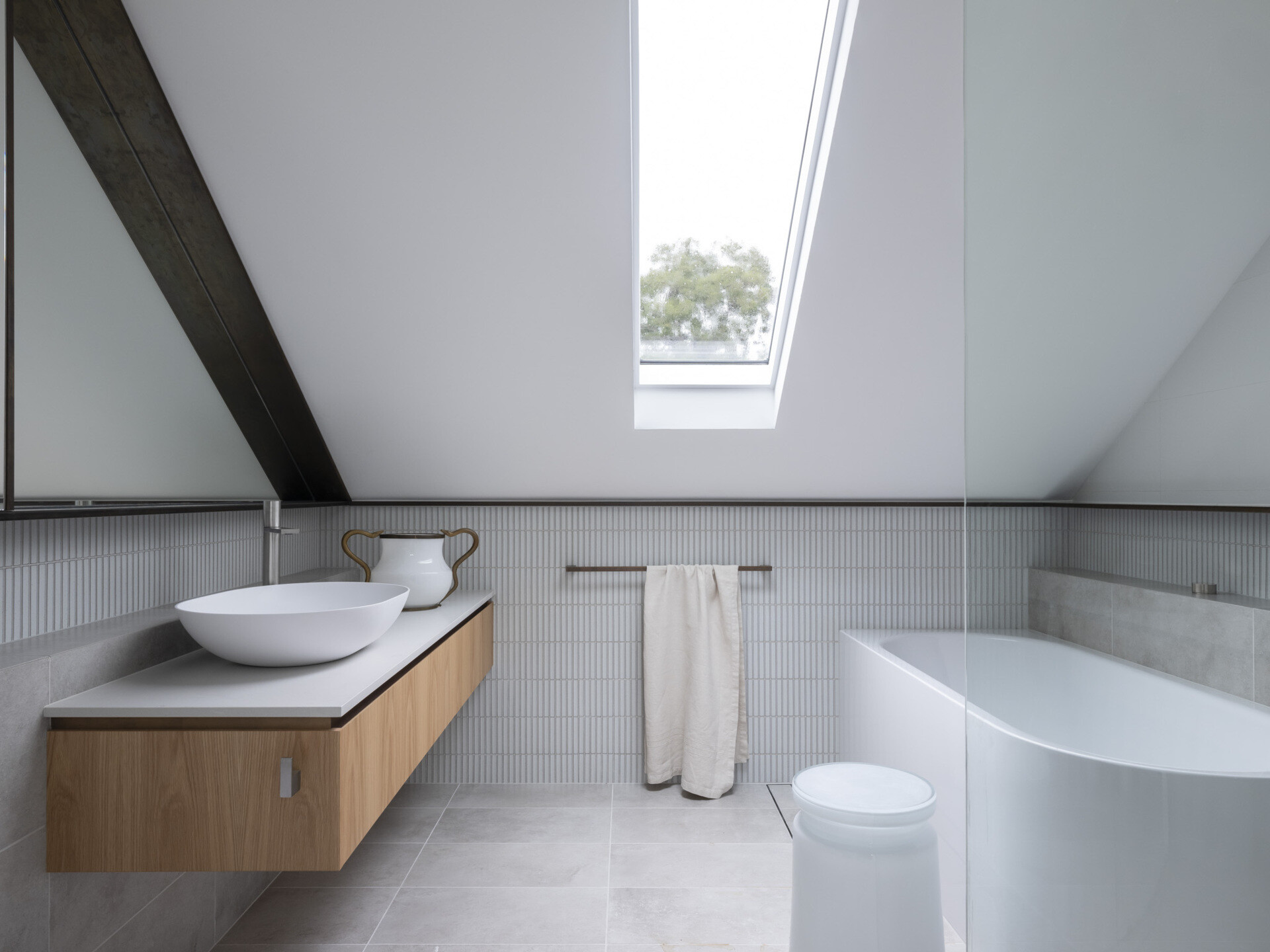 A modern white bathroom with a sloped ceiling and skylight.